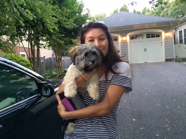A young woman holding a small dog in front of a house