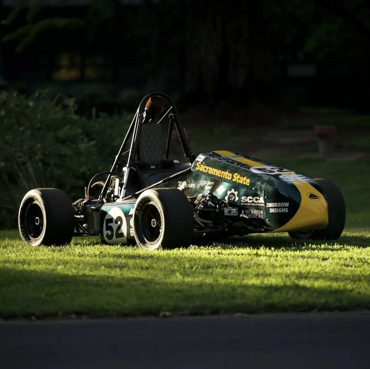 An open-wheel race car parked on a grassy area, with a Sacramento State and other sponsor logos visible on the side, numbered 52.