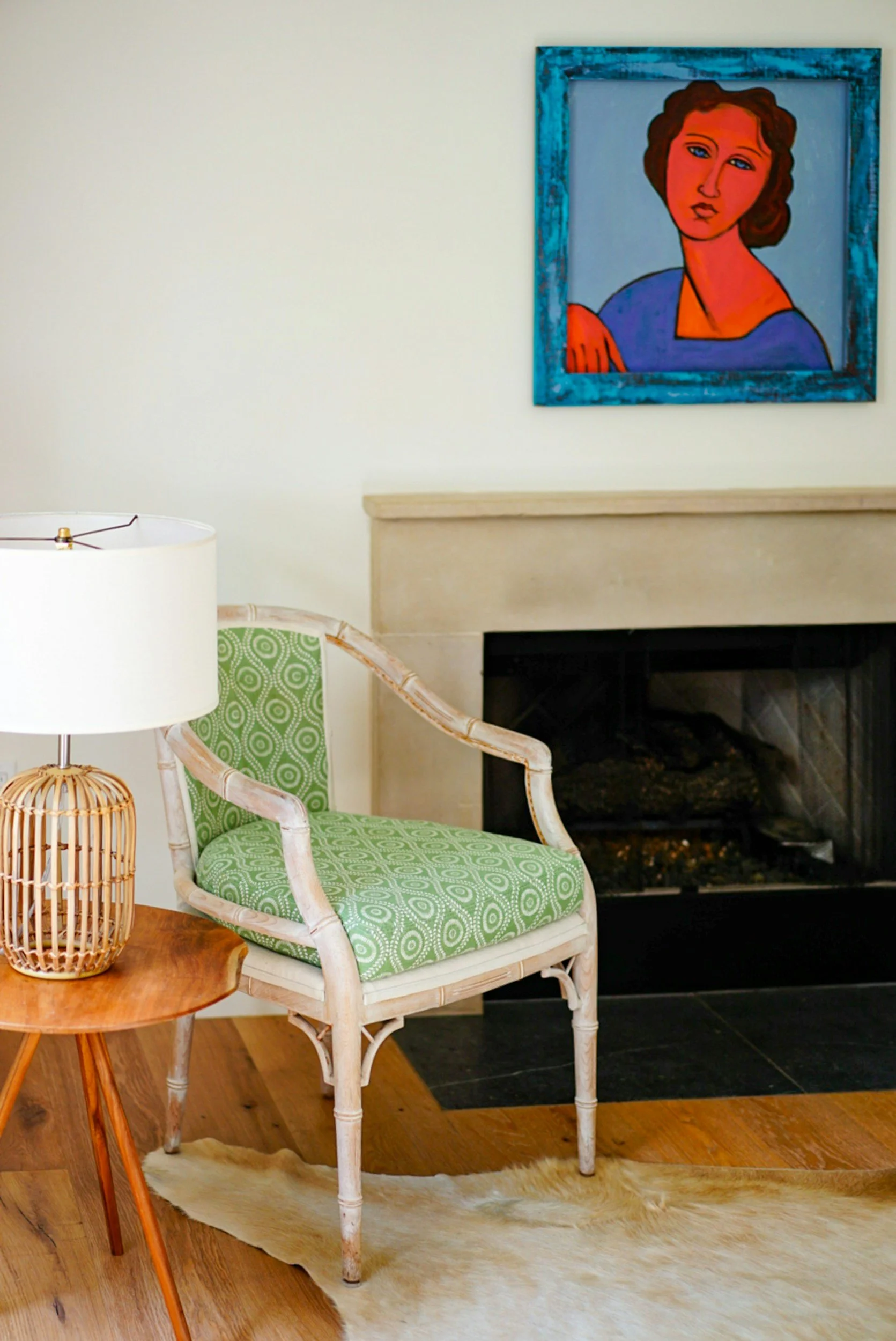 Hotel Room interior with a patterned green chair, wooden side table with lamp, fireplace, and abstract portrait painting.