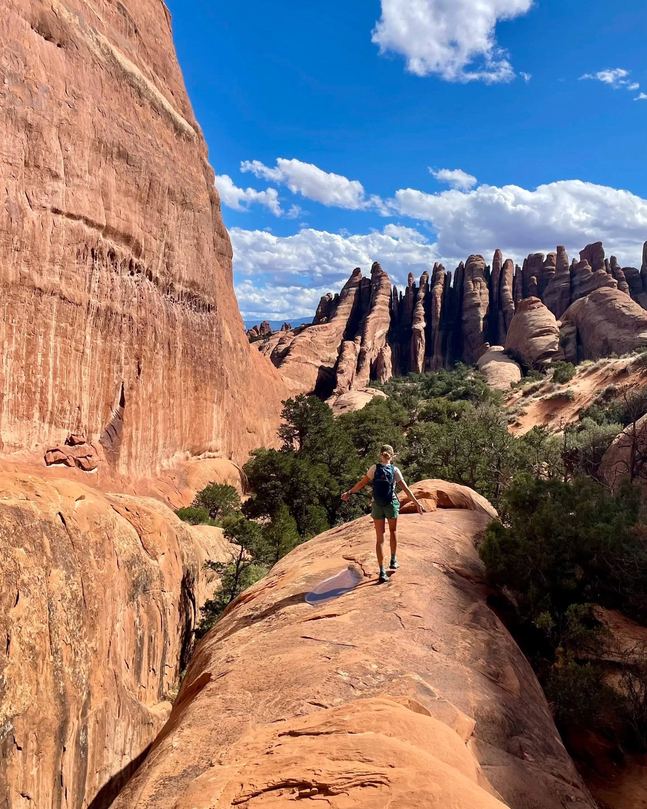Photo of a narrow, winding sandstone canyon with smooth, layered walls in shades of red and orange, illuminated by sunlight filtering through the top opening.