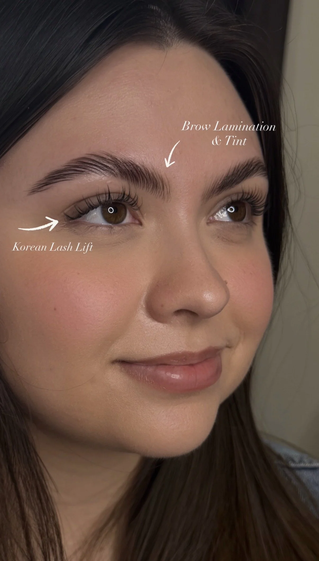 Close-up of a woman’s face, highlighting her well-groomed eyebrows with brow lamination and tint, and her eyelashes with Korean lash lift. Her skin is smooth and she has a slight smile.