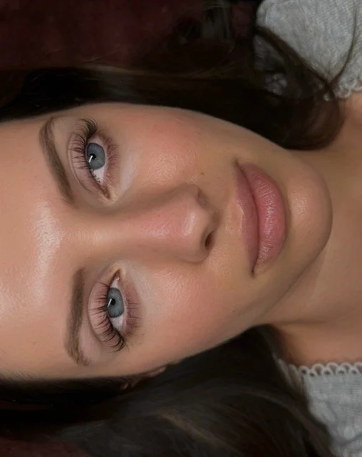 Close-up of a person's eye with long eyelashes, blue iris, and well-groomed eyebrow.
