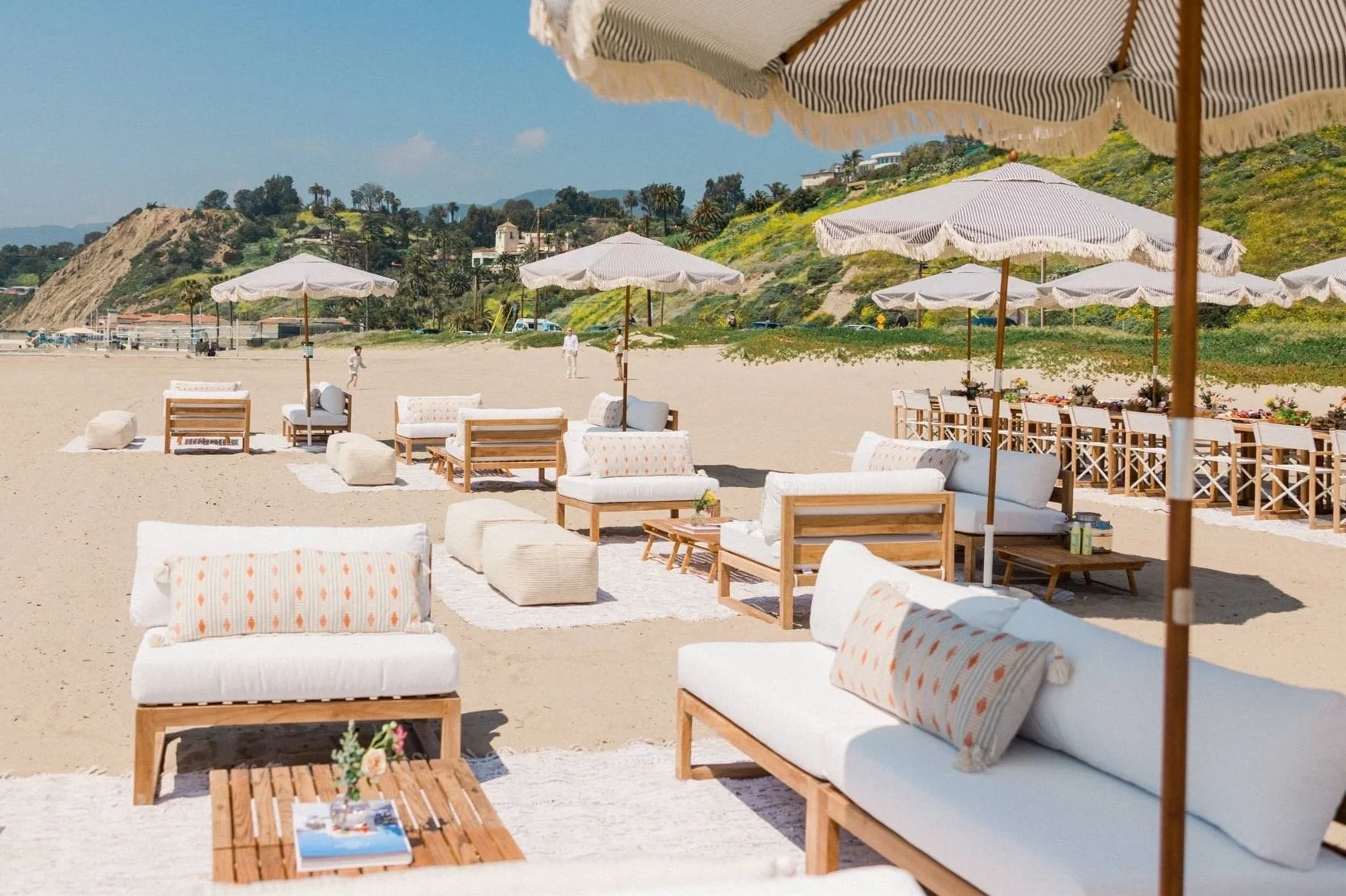 Wedding welcome party on the beach with lounge seating area rugs umbrellas and outdoor dining tables