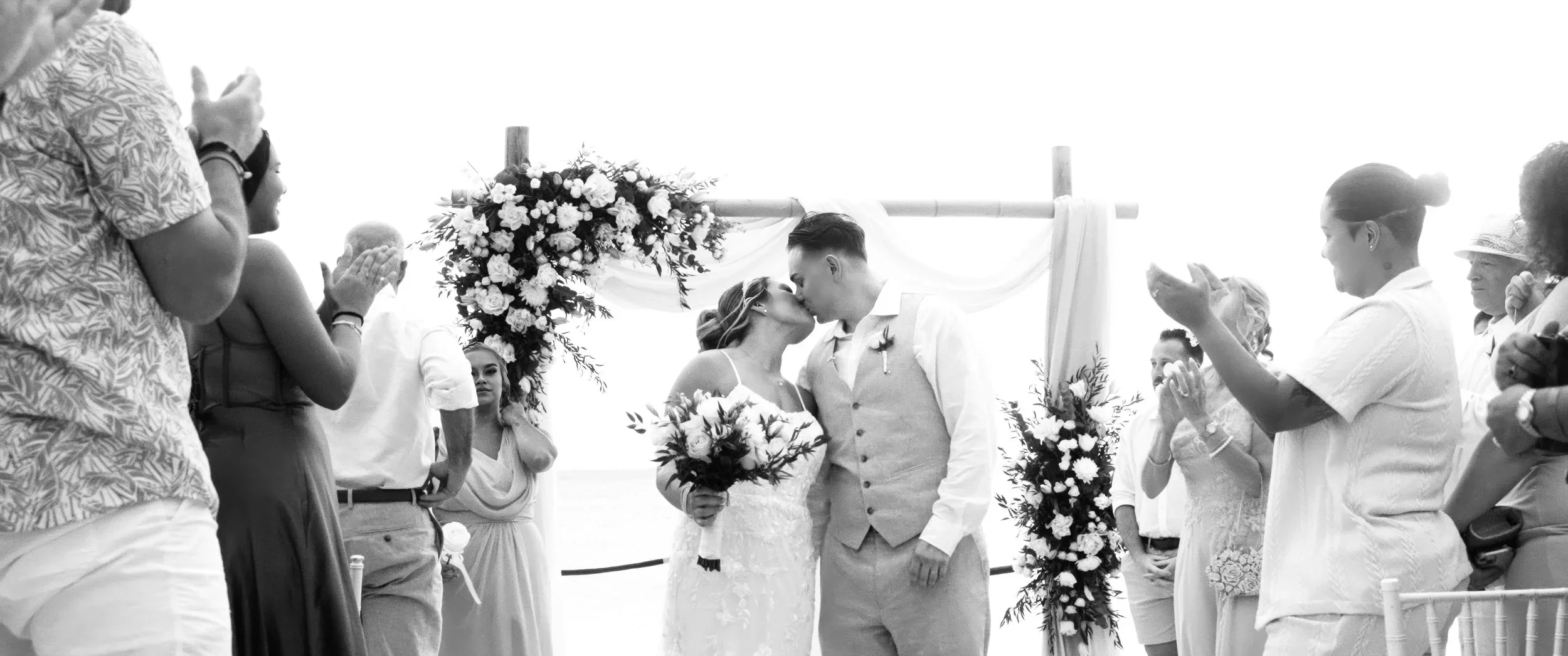 Aruba bride and groom kissing under a floral arch surrounded by guests at their destination wedding in Aruba
