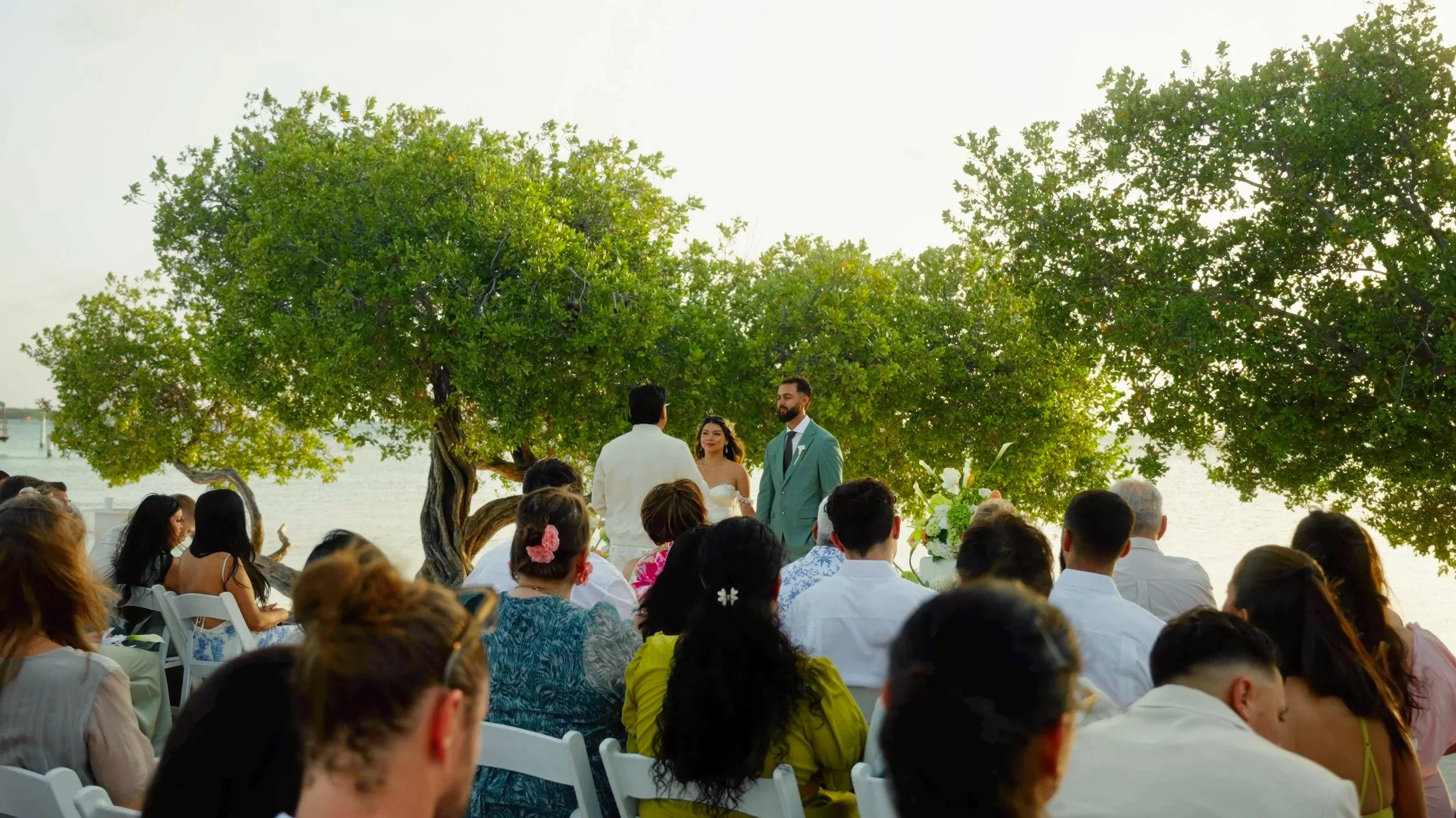 Beach wedding ceremony at sunset on Surfside Beach, Aruba with guests and floral arch, destination wedding videography by Wedding Films by Mira