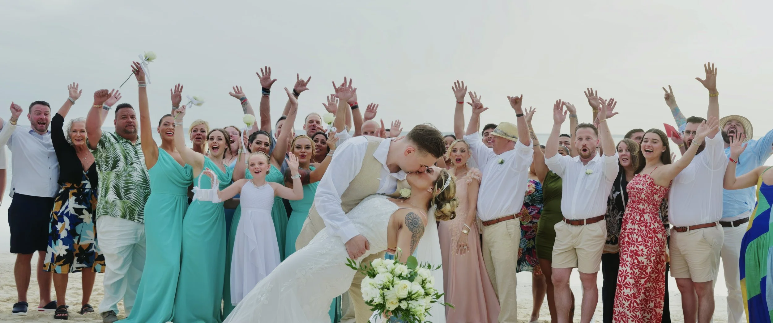 Aruba wedding couple Gianna and Daniel kissing on the beach as their guests celebrate at their Holiday Inn Resort Aruba wedding in Palm Beach