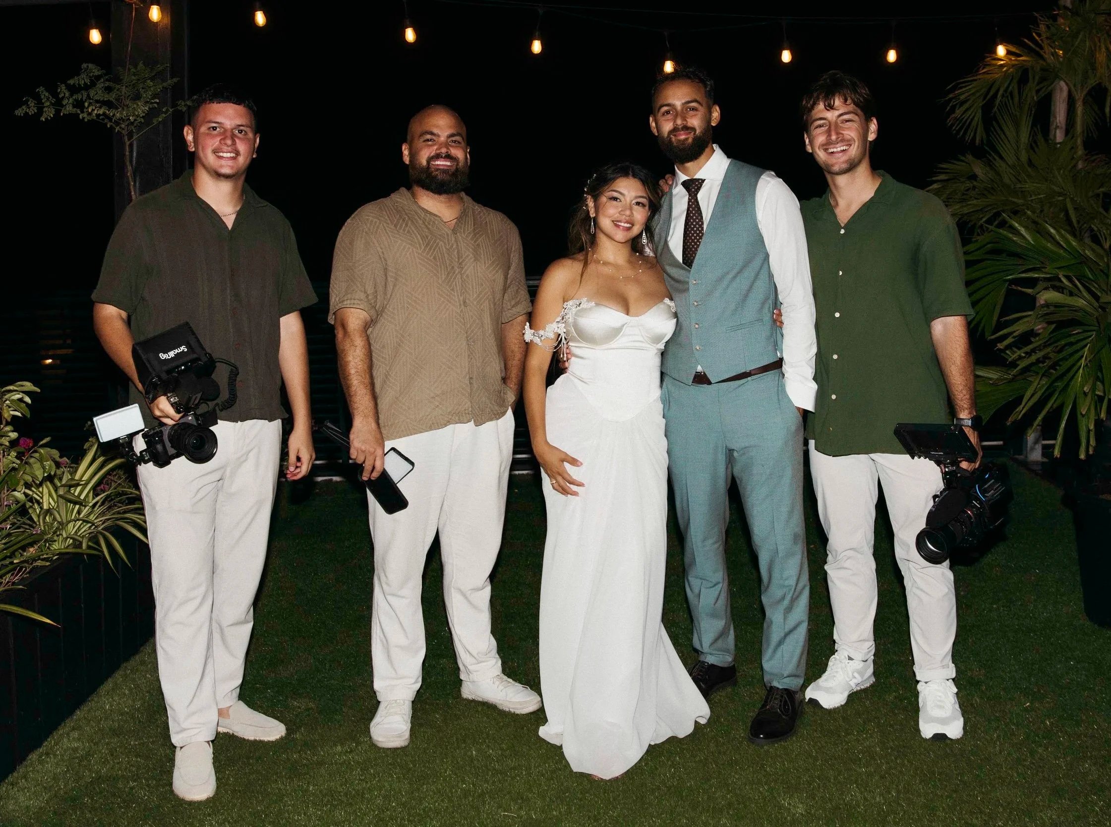 Aruba wedding videographers from Wedding Films by Mira posing with newlyweds at night at an Aruba destination wedding