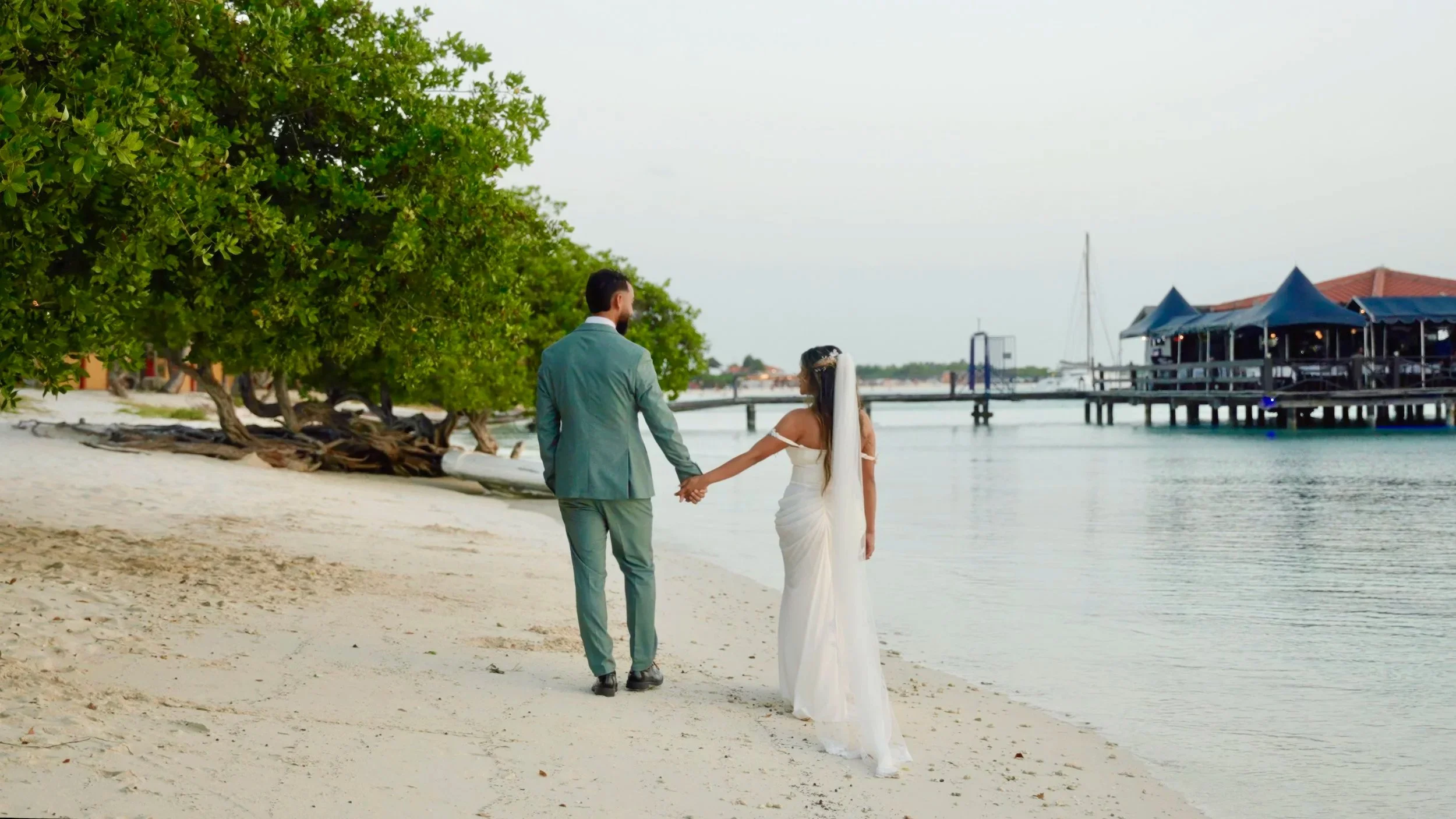 Aruba bride and groom walking hand in hand on Surfside Beach by the marina in Oranjestad, Aruba, filmed by Aruba wedding videographer Wedding Films by Mira
