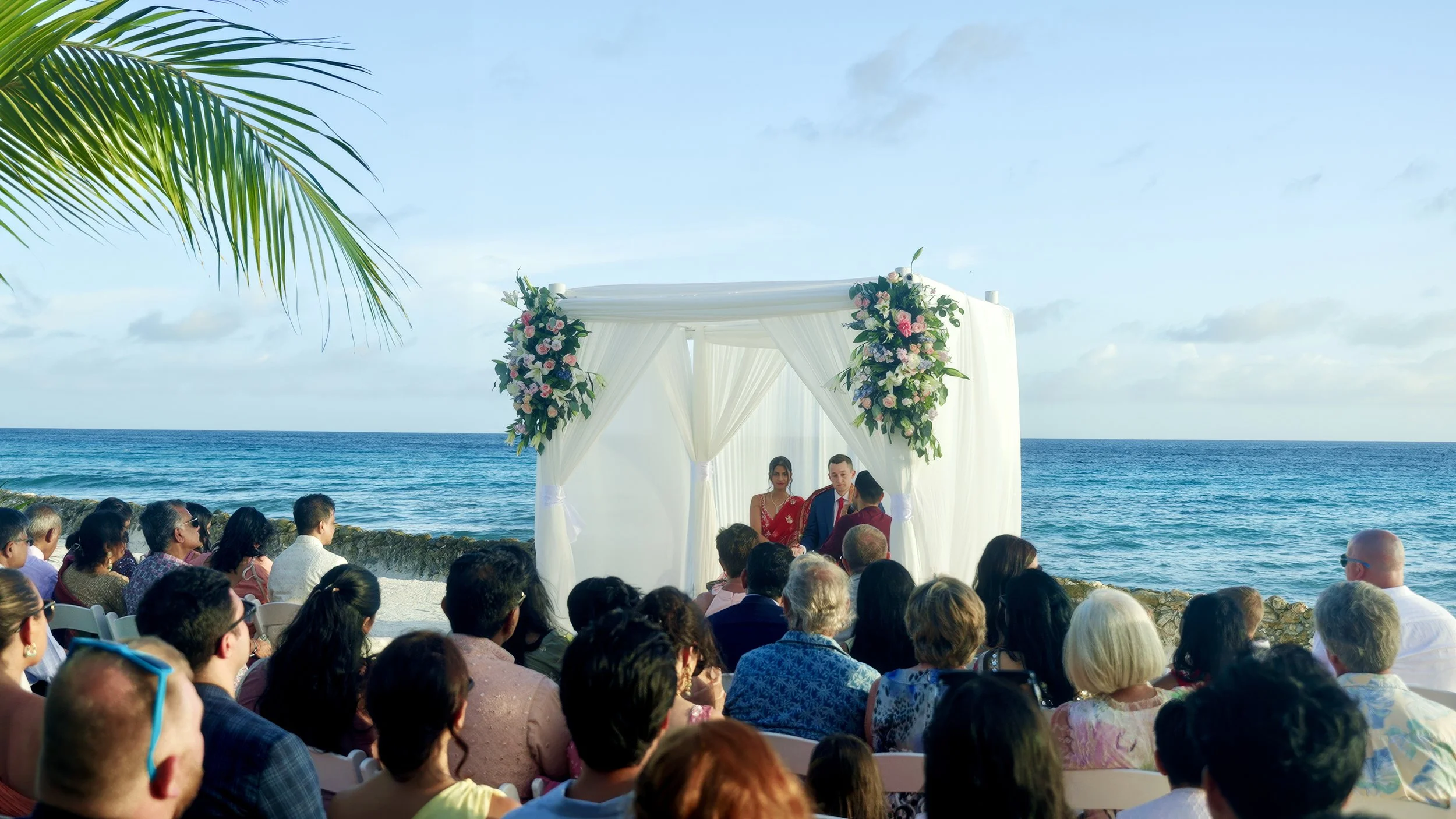 Aruba wedding couple exchanging vows under a white floral arch by the ocean at Renaissance Private Flamingo Island, Aruba