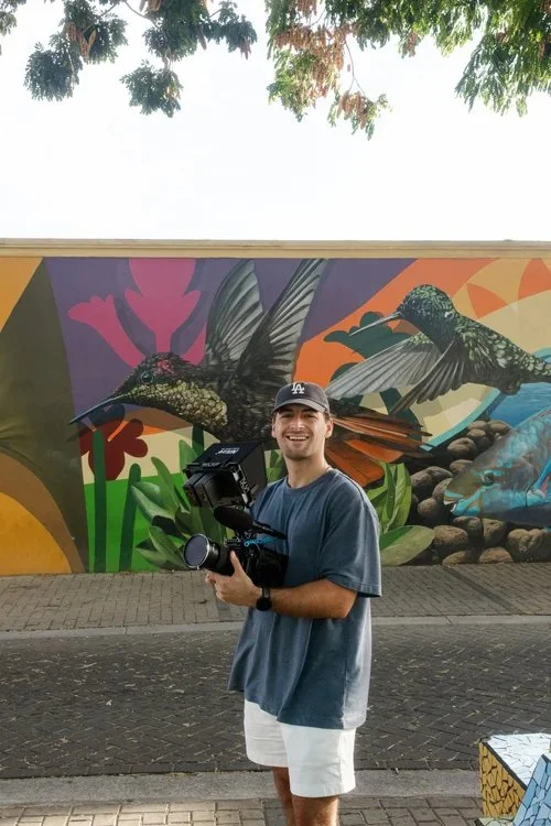 Aruba wedding filmmaker Tyler Cavallaro with his camera in front of a colorful Aruba street mural