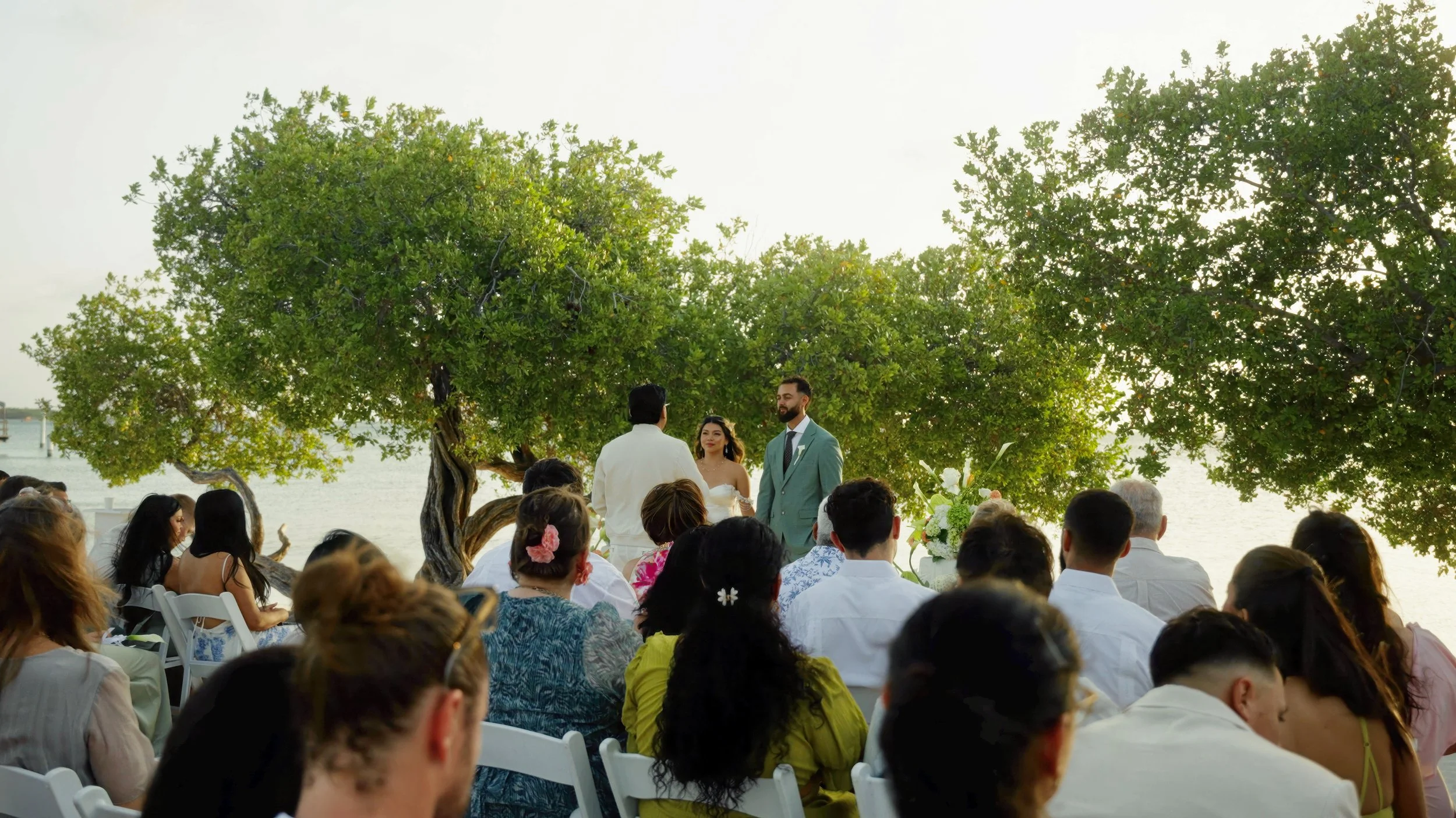 Beach wedding ceremony at sunset on Surfside Beach, Aruba with guests and floral arch, destination wedding videography by Wedding Films by Mira
