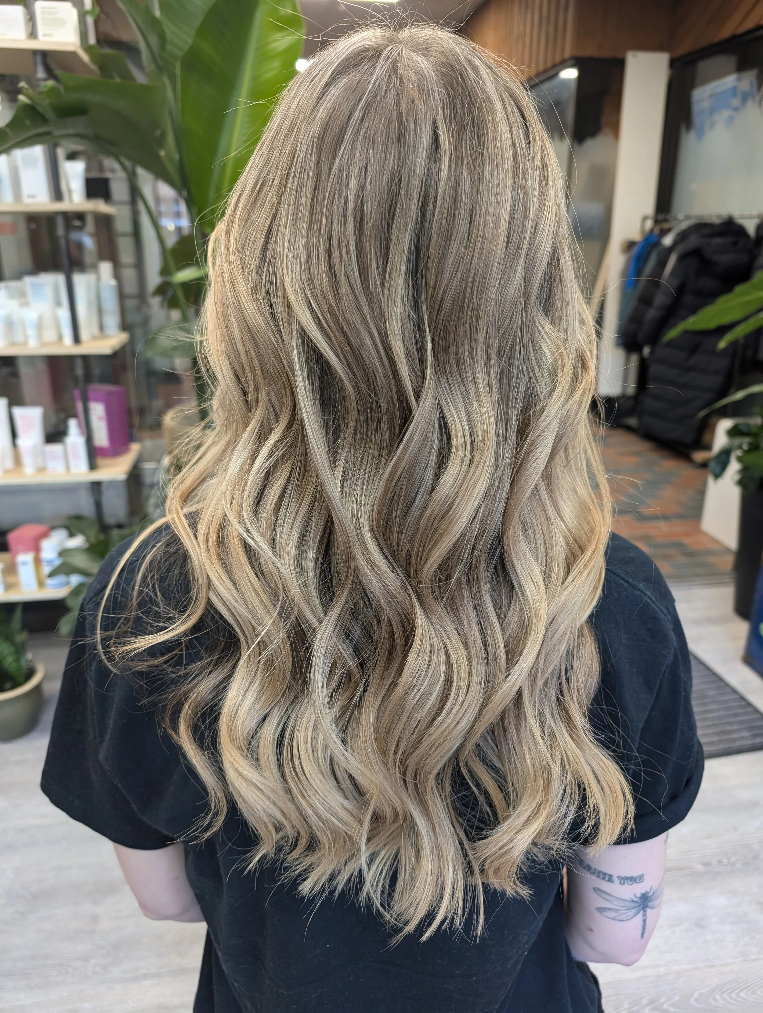 Back of a woman with long, blonde, wavy hair inside a salon or store.