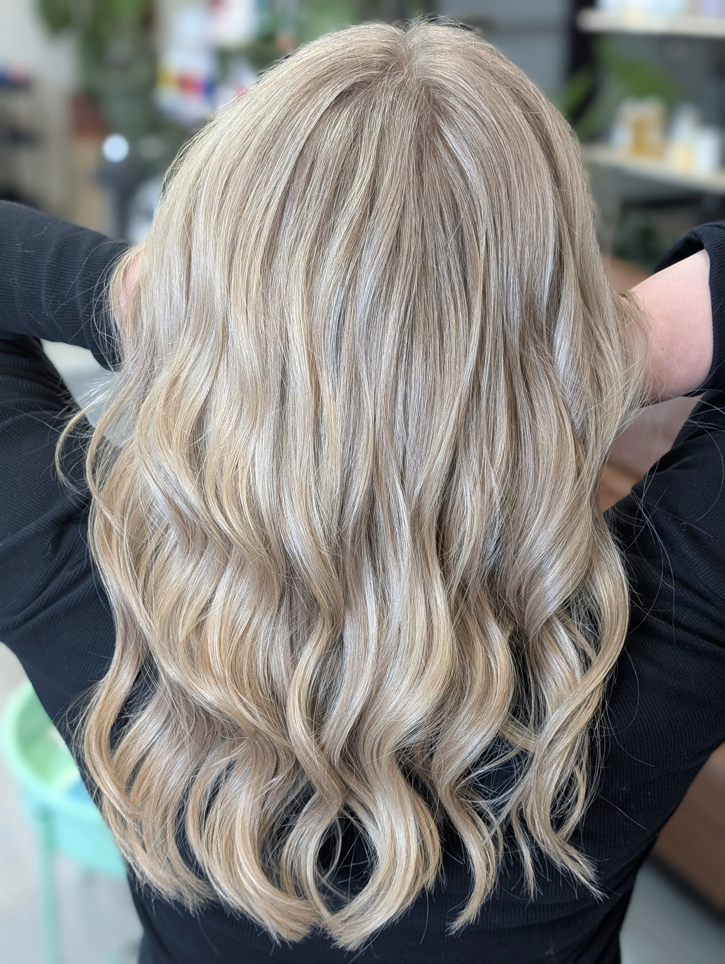Woman with long, wavy, blonde hair wearing a black shirt in an indoor setting.