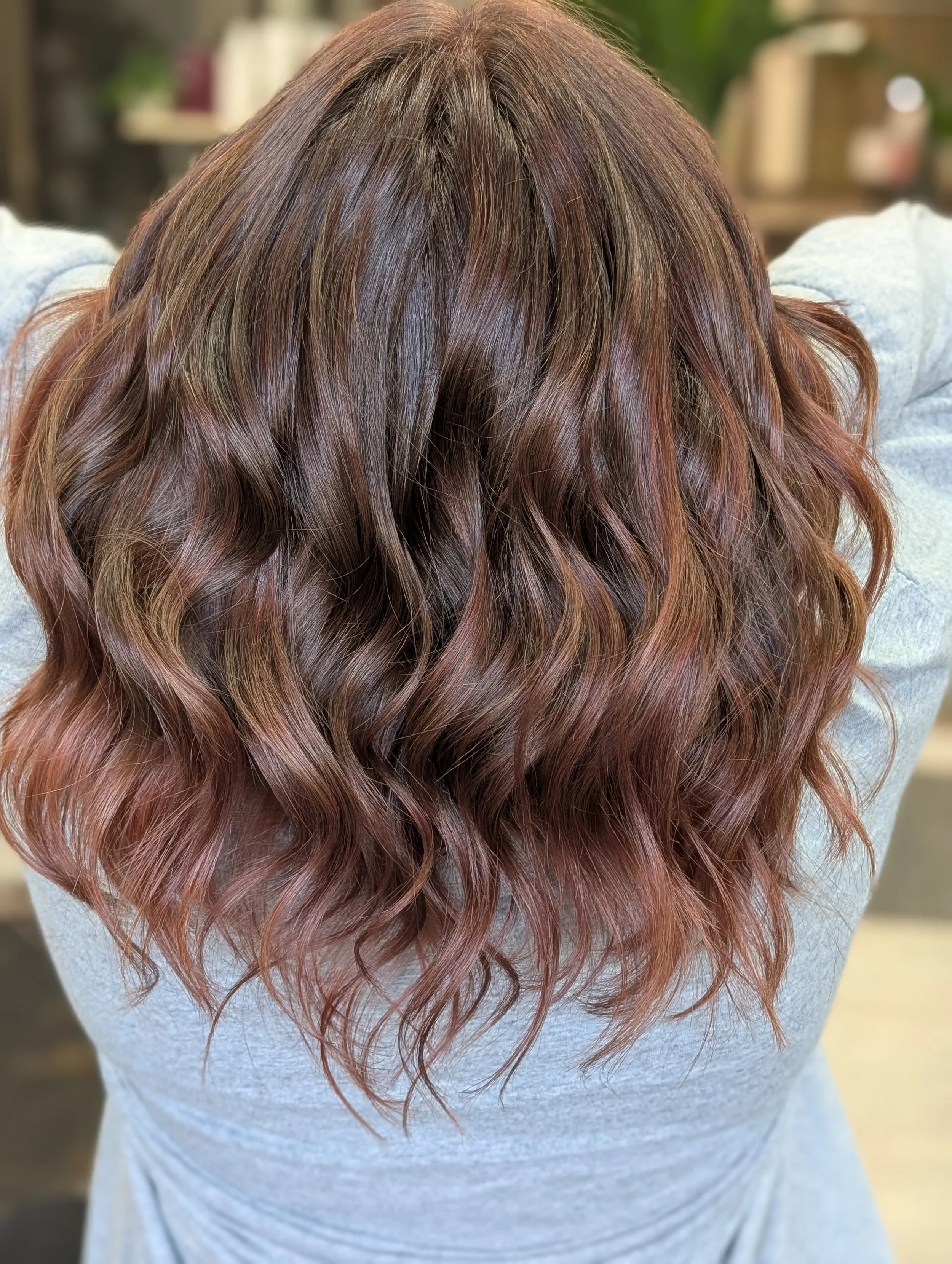 Back of a person's head with wavy, shoulder-length, reddish-brown hair.