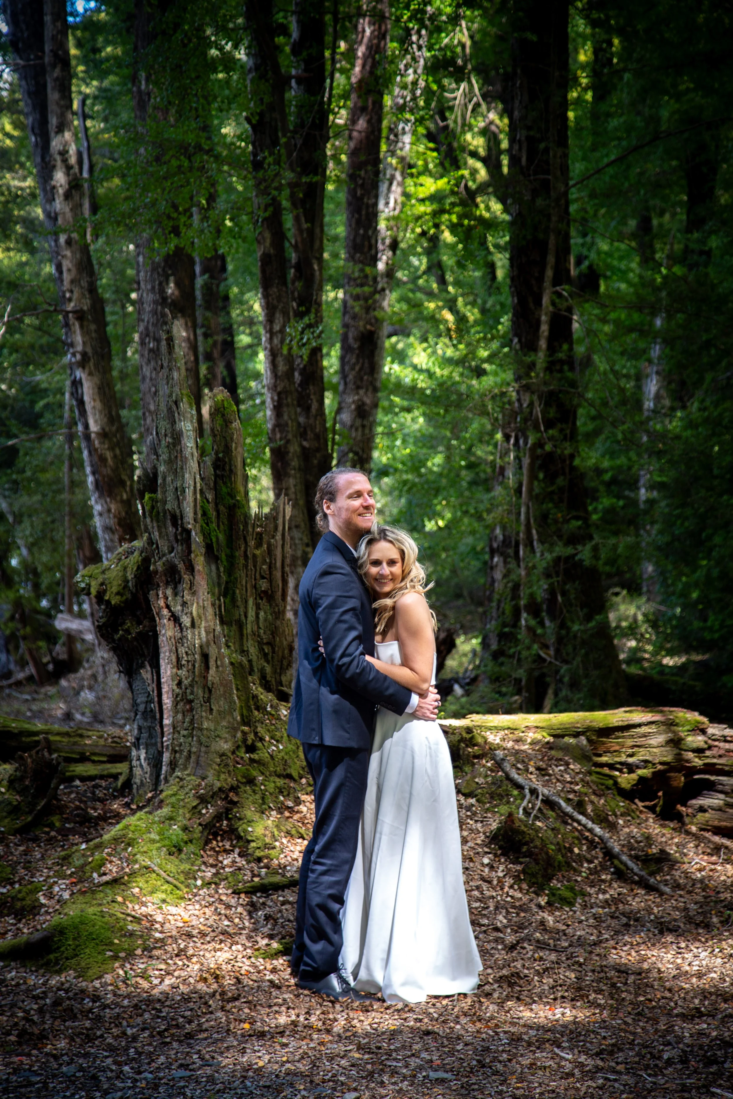 A couple in wedding attire embracing in a lush, green forest.