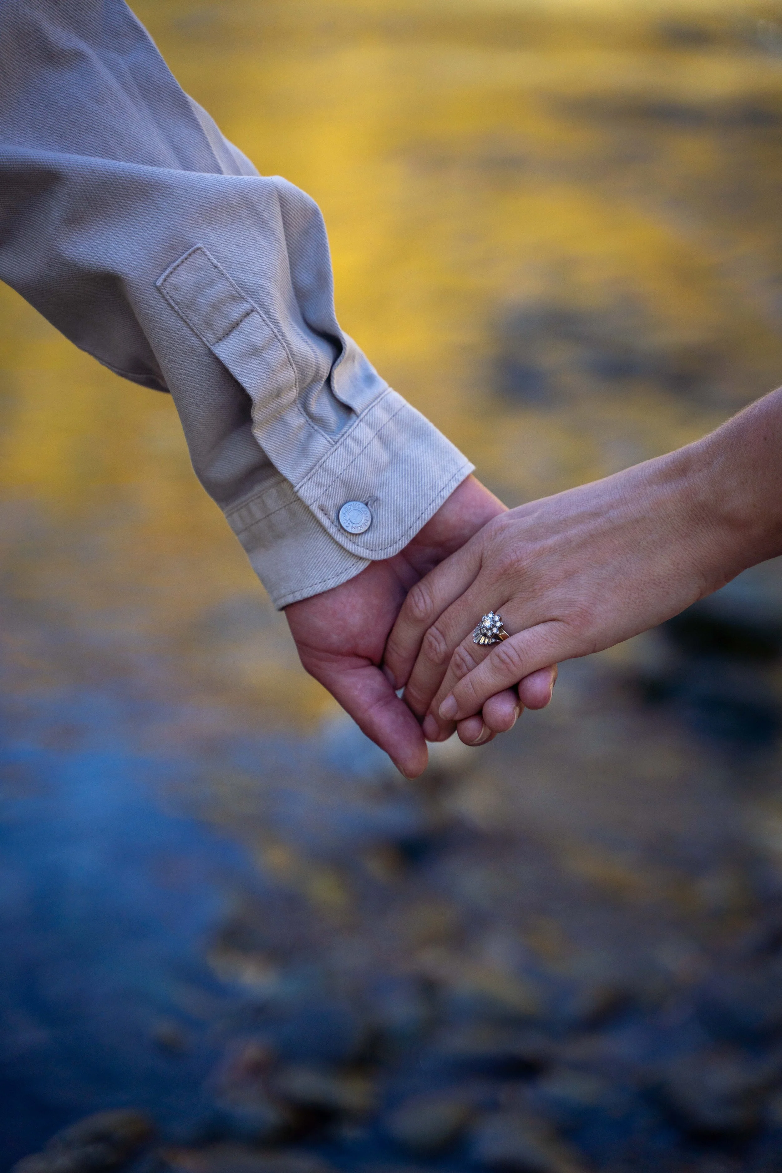 Close-up of a couple holding hands with a wedding ring, with water in the background.