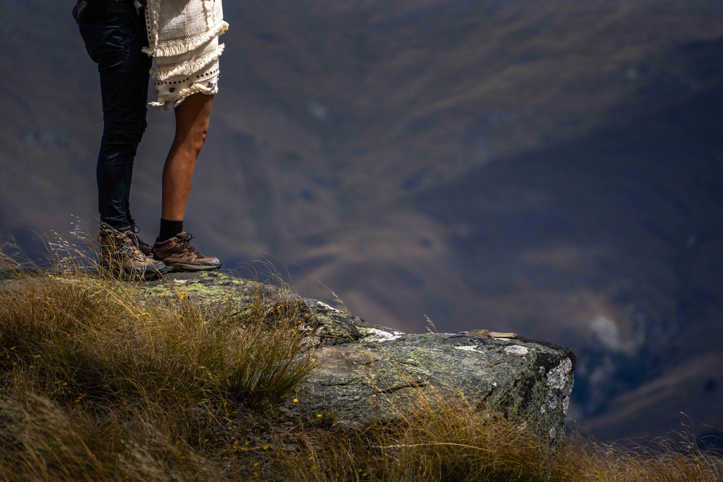 Two hikers standing on a rocky ledge overlooking a mountain landscape.