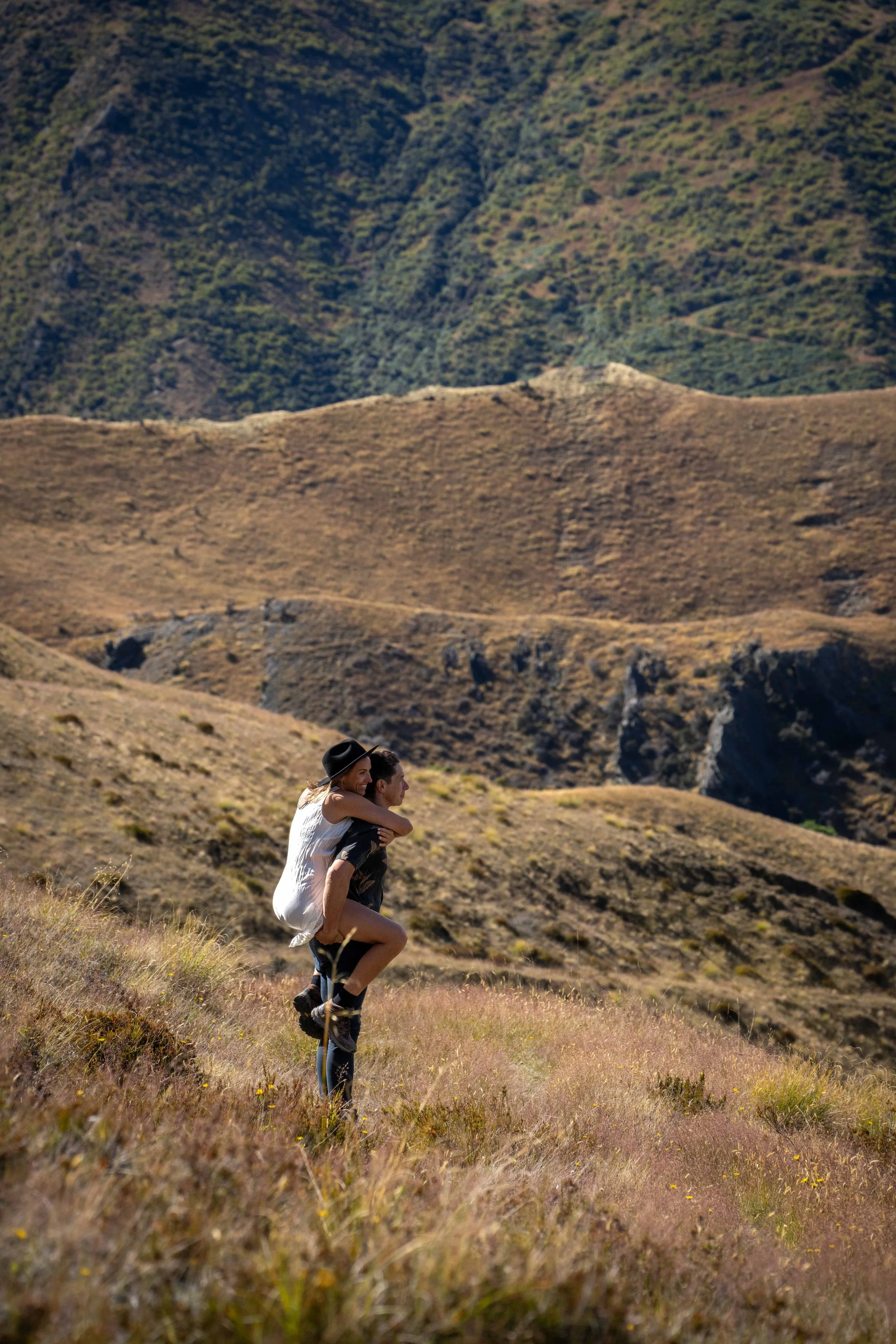 A couple outdoors in a mountainous landscape, with the man giving the woman a piggyback ride.