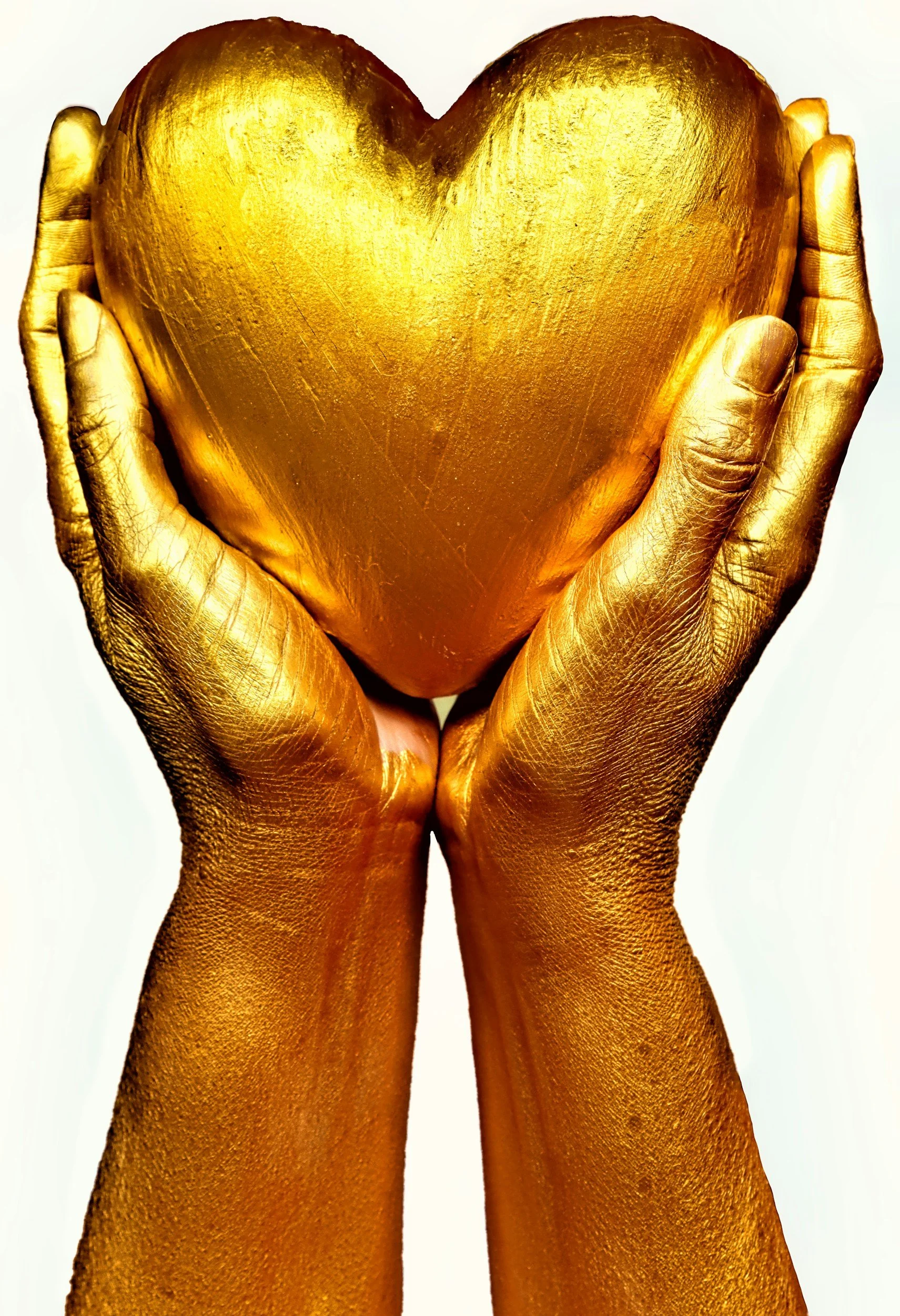 Hands holding a golden heart sculpture on a white background.