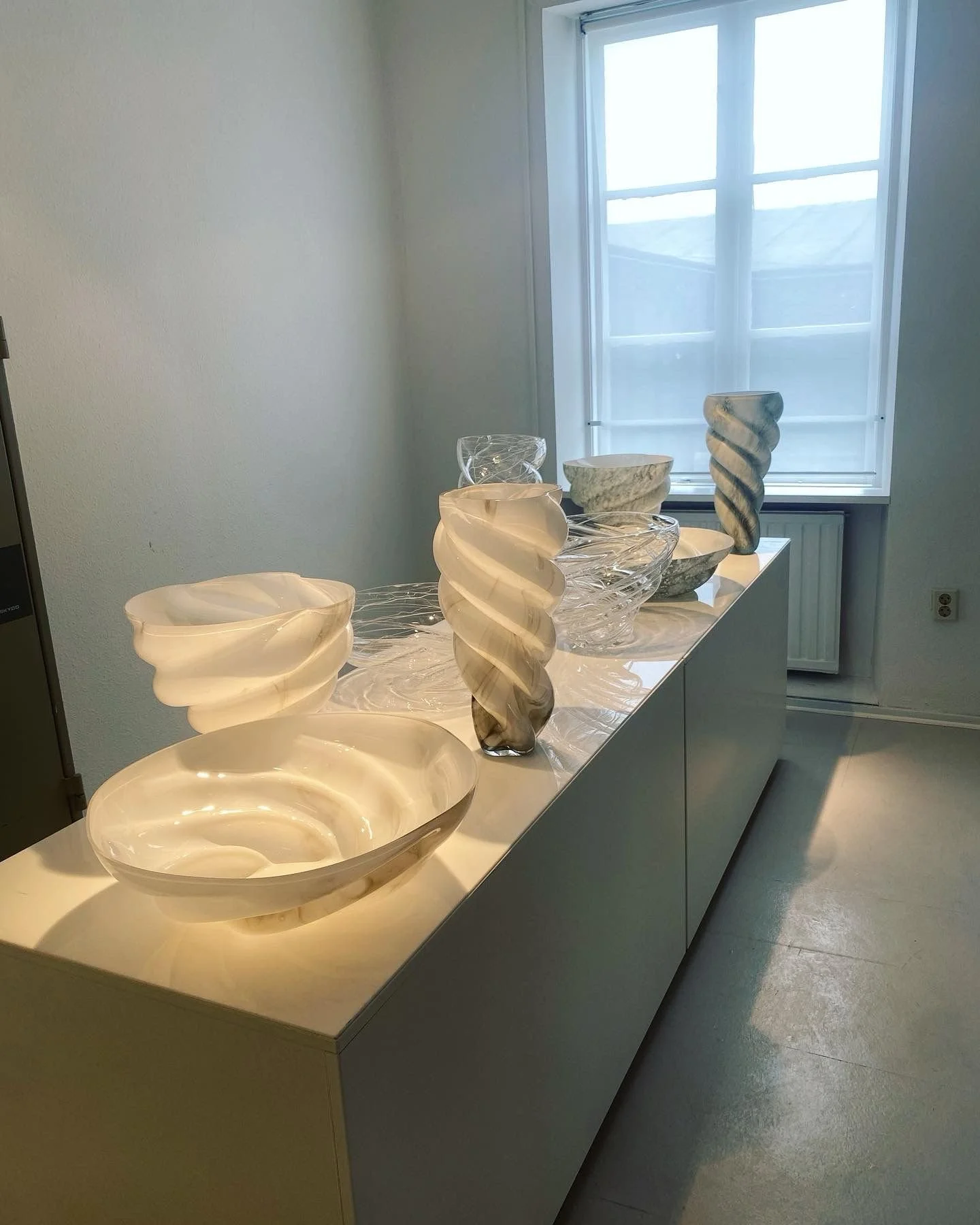 Display of illuminated onyx or marble bowls and vases on a white cabinet near a window