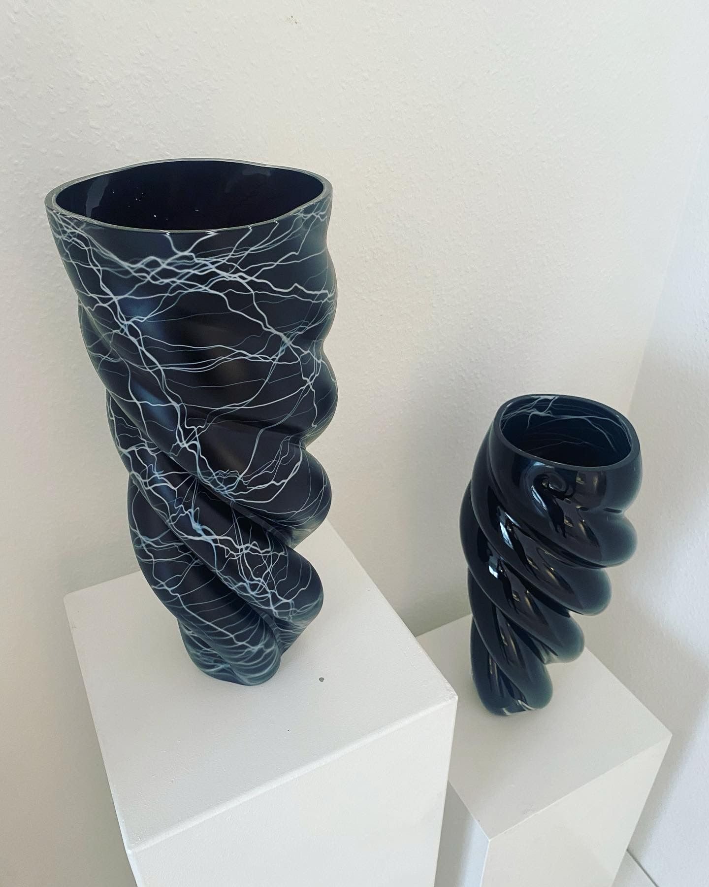 Two abstract black ceramic sculptures with white lightning patterns on white pedestals.