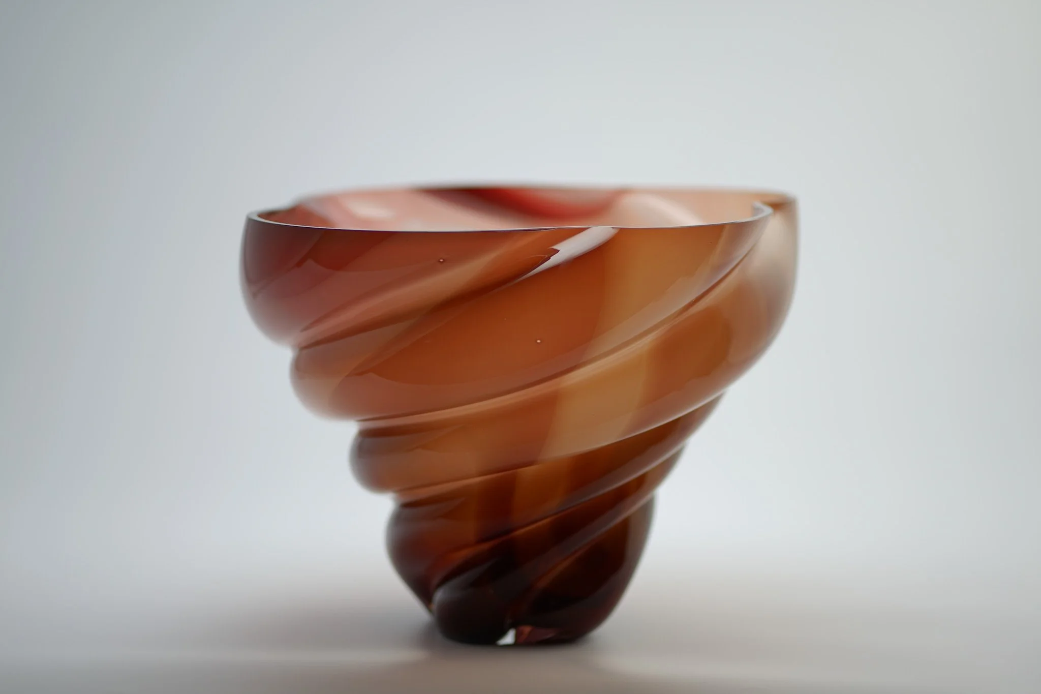 A close-up image of a spiral-shaped glass bowl with swirled red and orange hues against a plain white background.