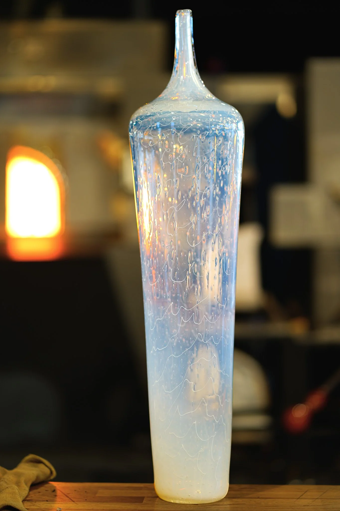 A decorative glass vase with a narrow neck and curvy patterns, standing on a wooden surface with a blurred background.