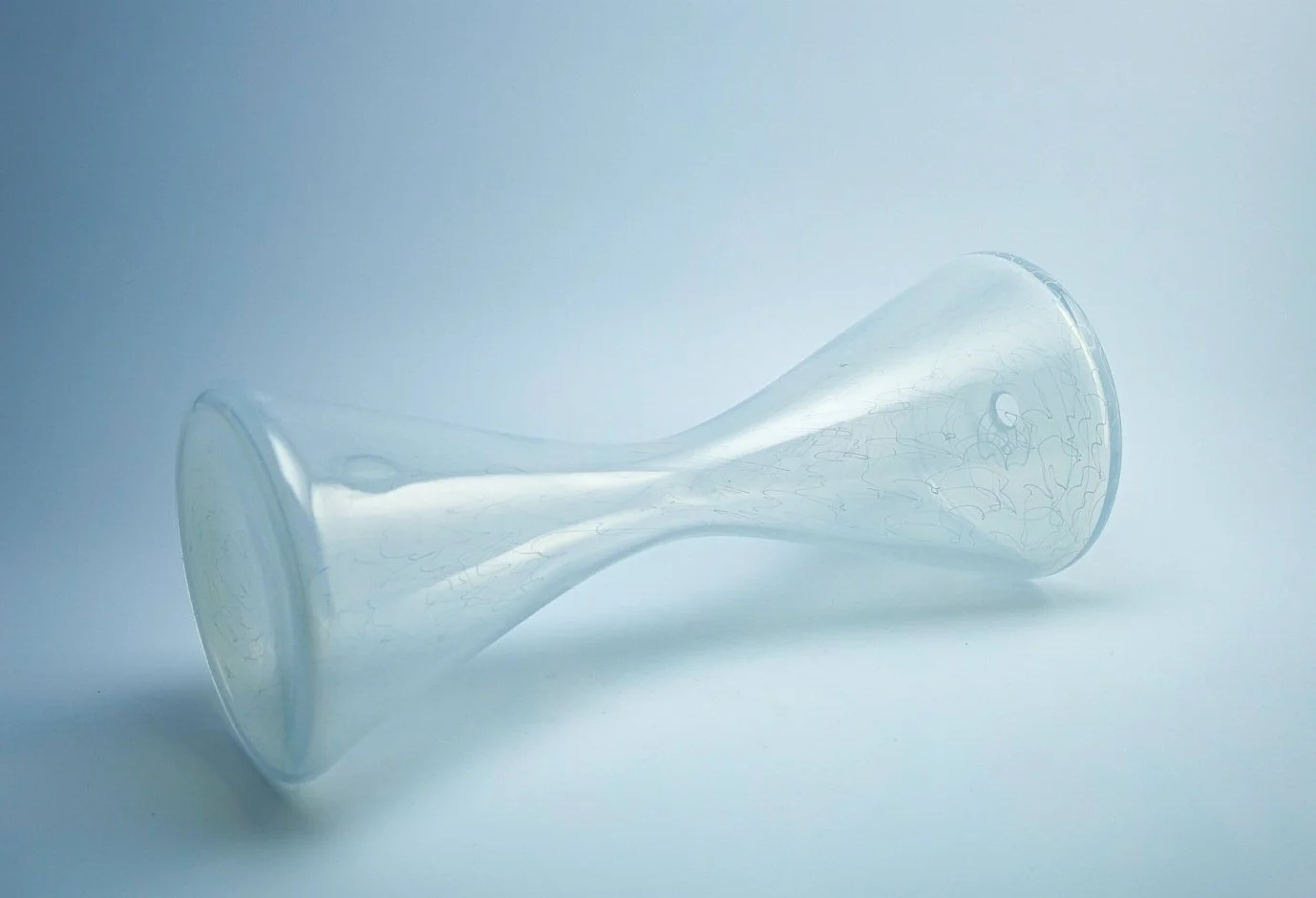 A glass vase lying on its side on a white surface with a light background.