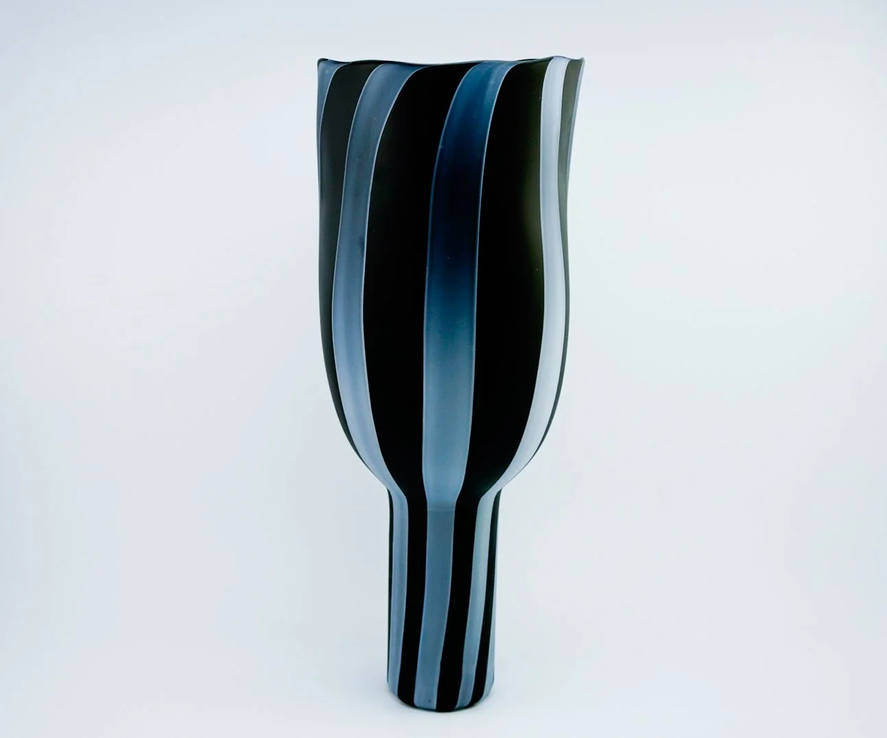Black and white striped modern glass vase with a wavy design, set against a plain light background.