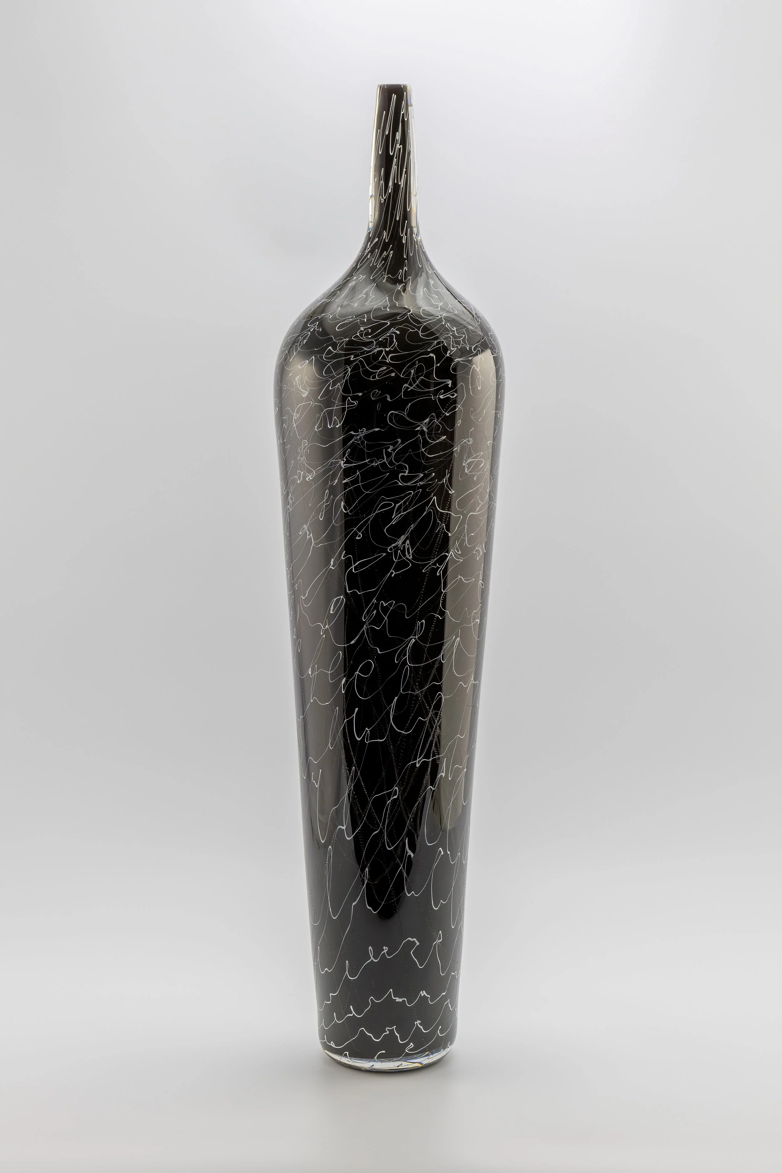 Black glass vase with white squiggly line design, tall and slender with a narrow neck, set against a plain light grey background.