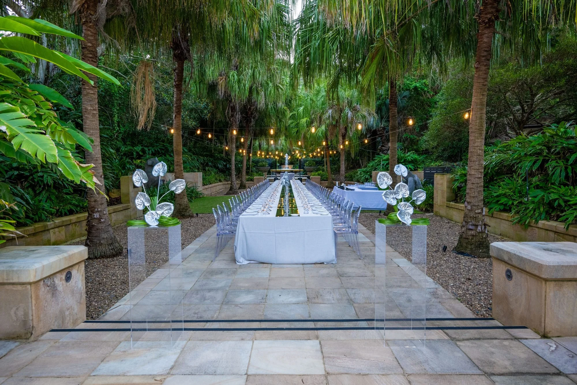 Palm-lined pathway with silver floral installations leading to an outdoor banquet table on Hayman Island