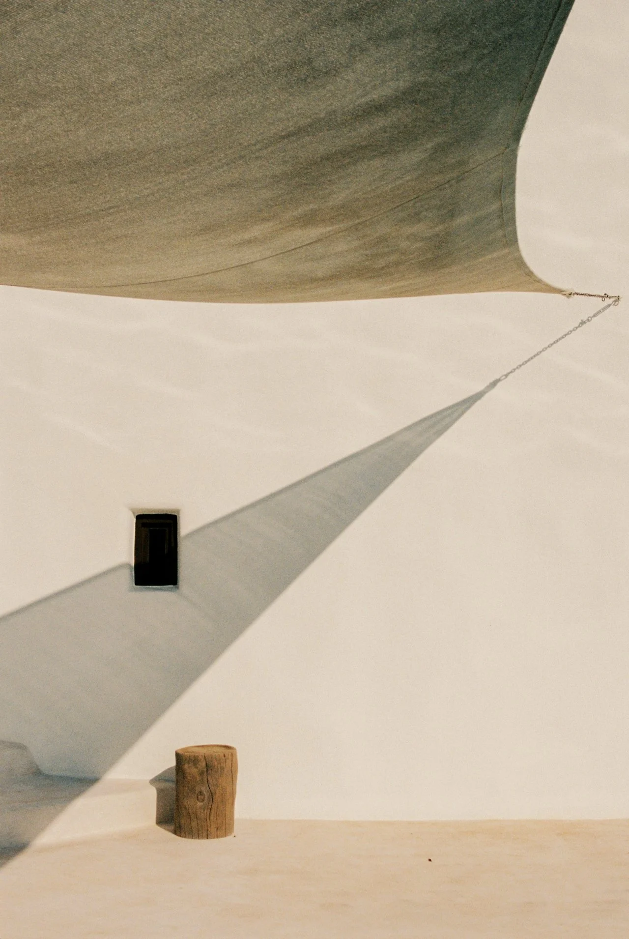Close-up of a boat's hull casting a shadow on the ground, with a wooden post and a small window on the white wall