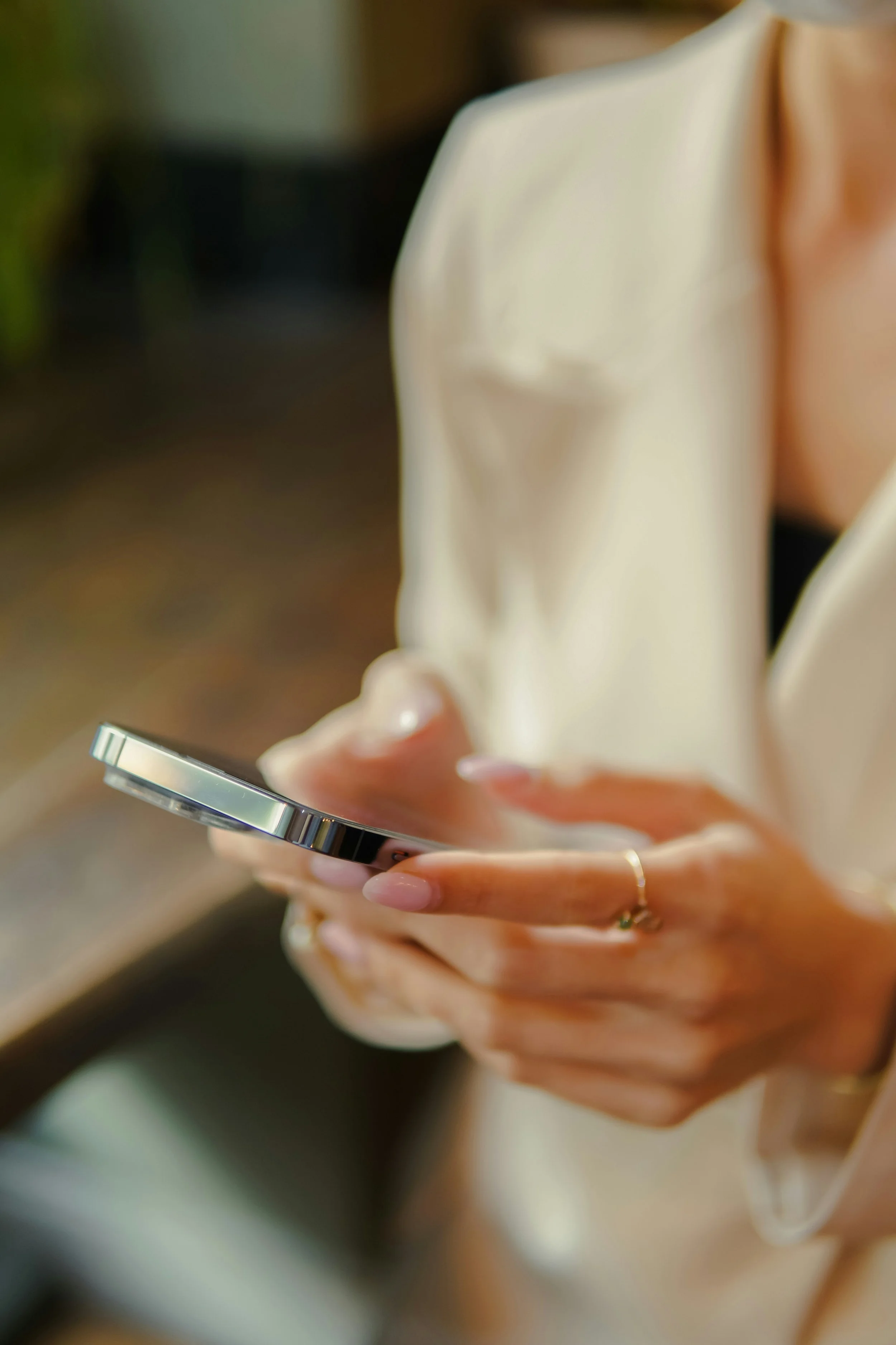 Person holding a smartphone with a light-colored satin blouse and light pink nails.