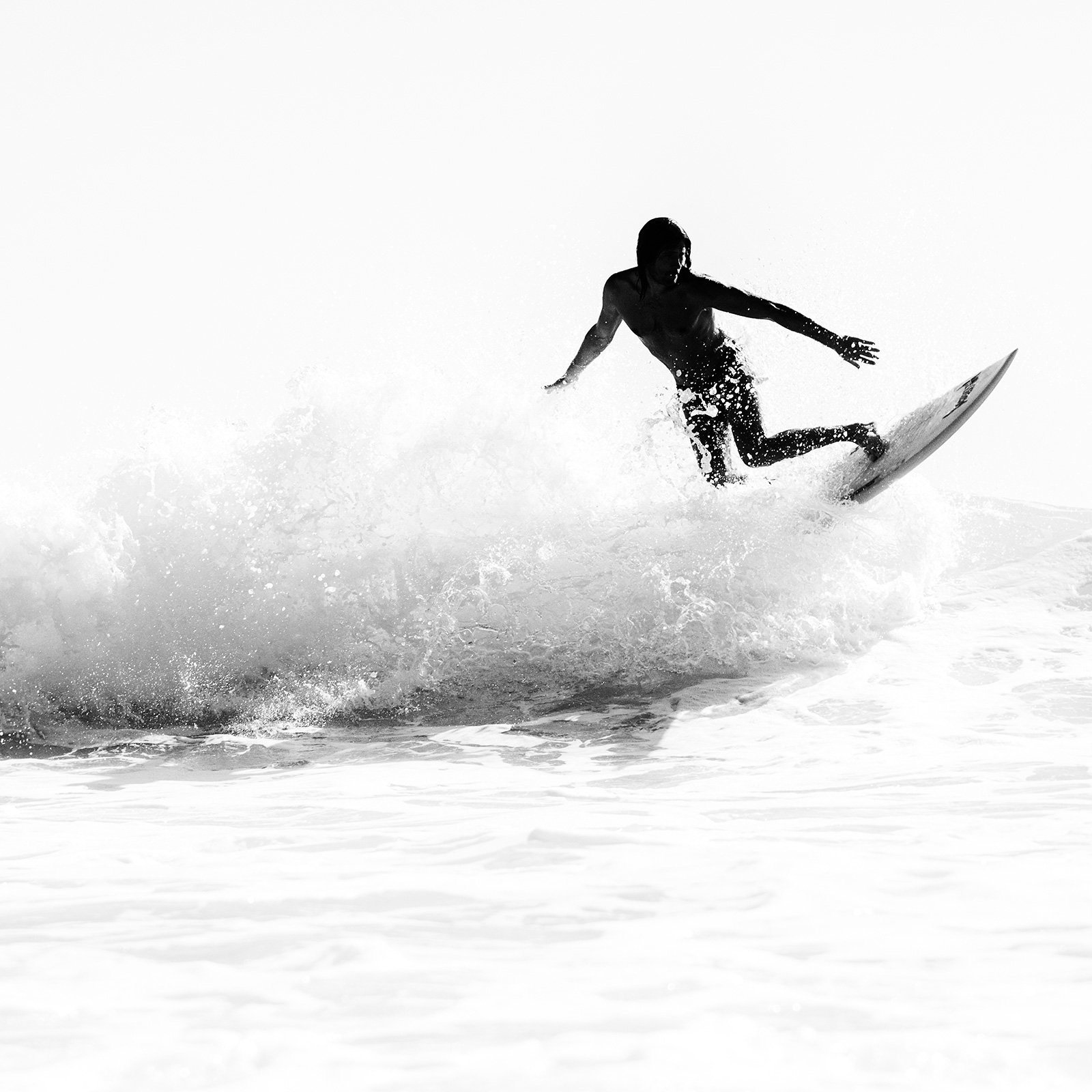 A large square black and white photographic print of a surfer in an animated dance like pose as he turns his surfboard on top of a wave