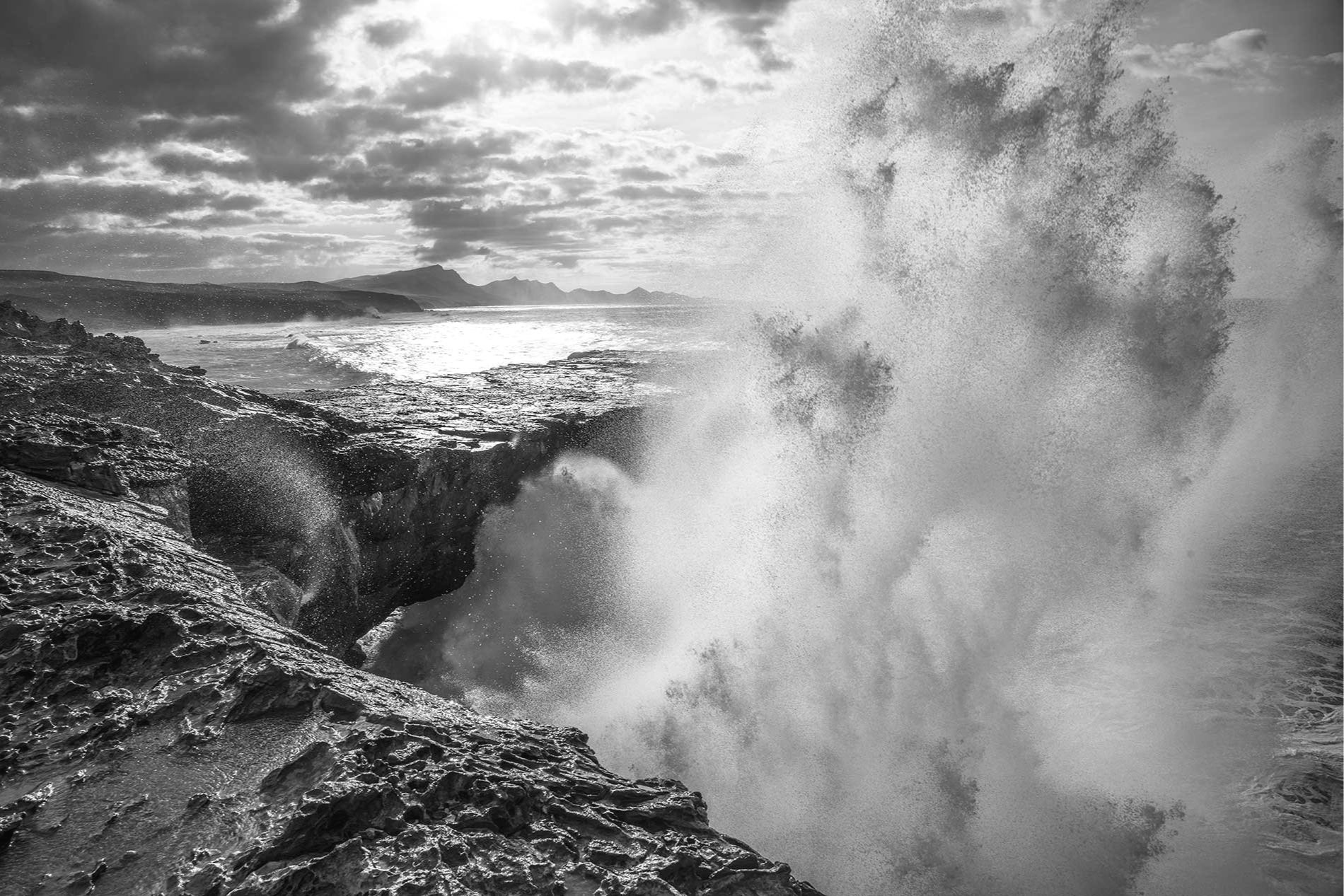 Large black and white photo print of an enormous wave crashing against cliffs