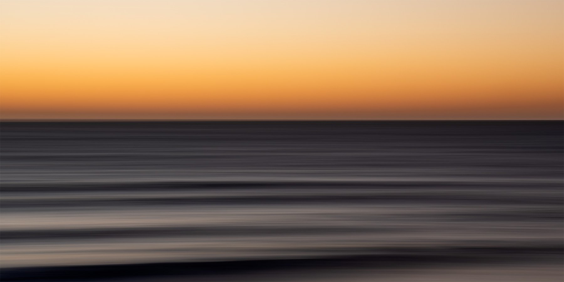A beautiful slow shutter photo print of a sunrise over the sea with soft pastel colors of orange and grey