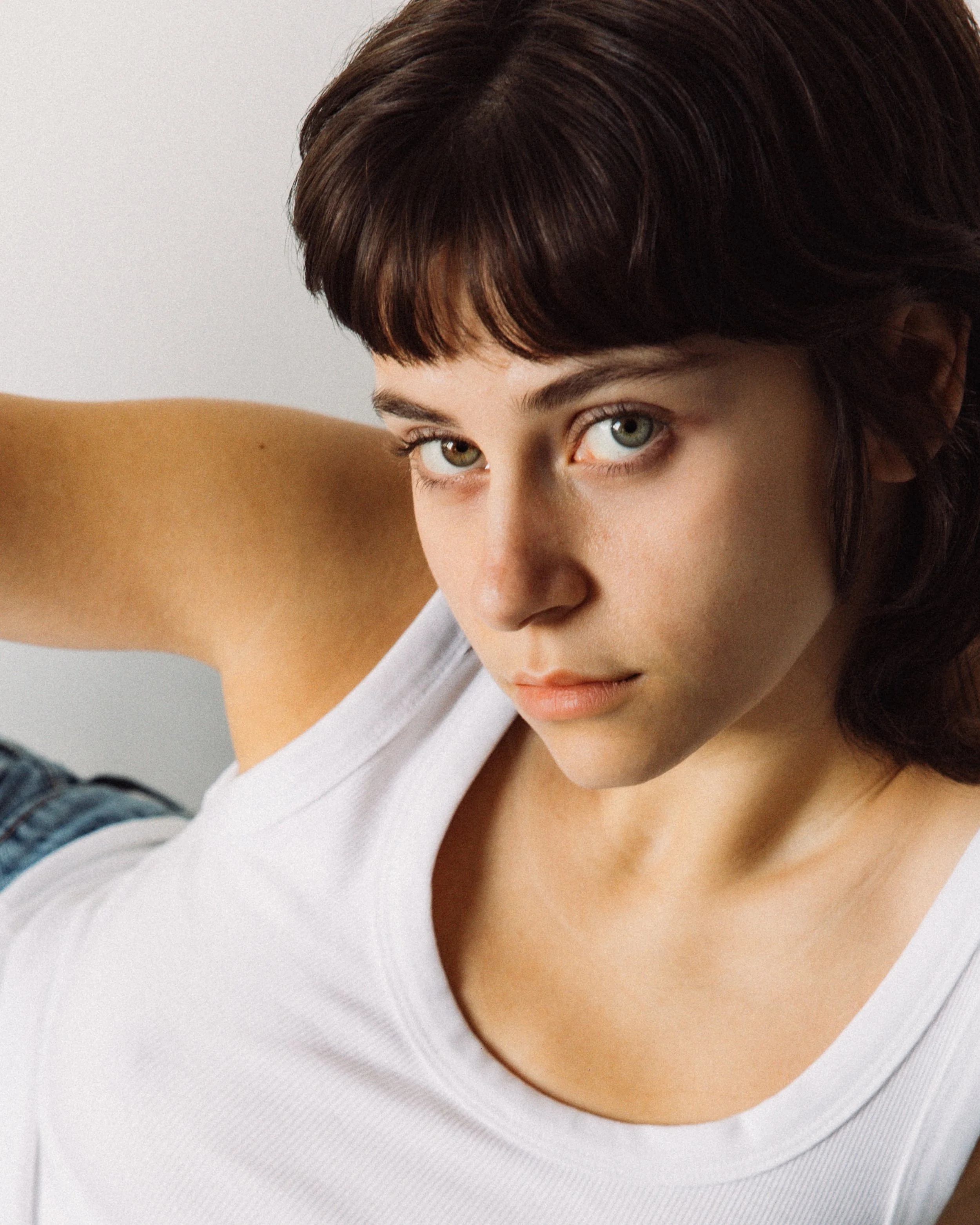 Close-up of a woman with short brown hair and blue eyes, wearing a white sleeveless top.