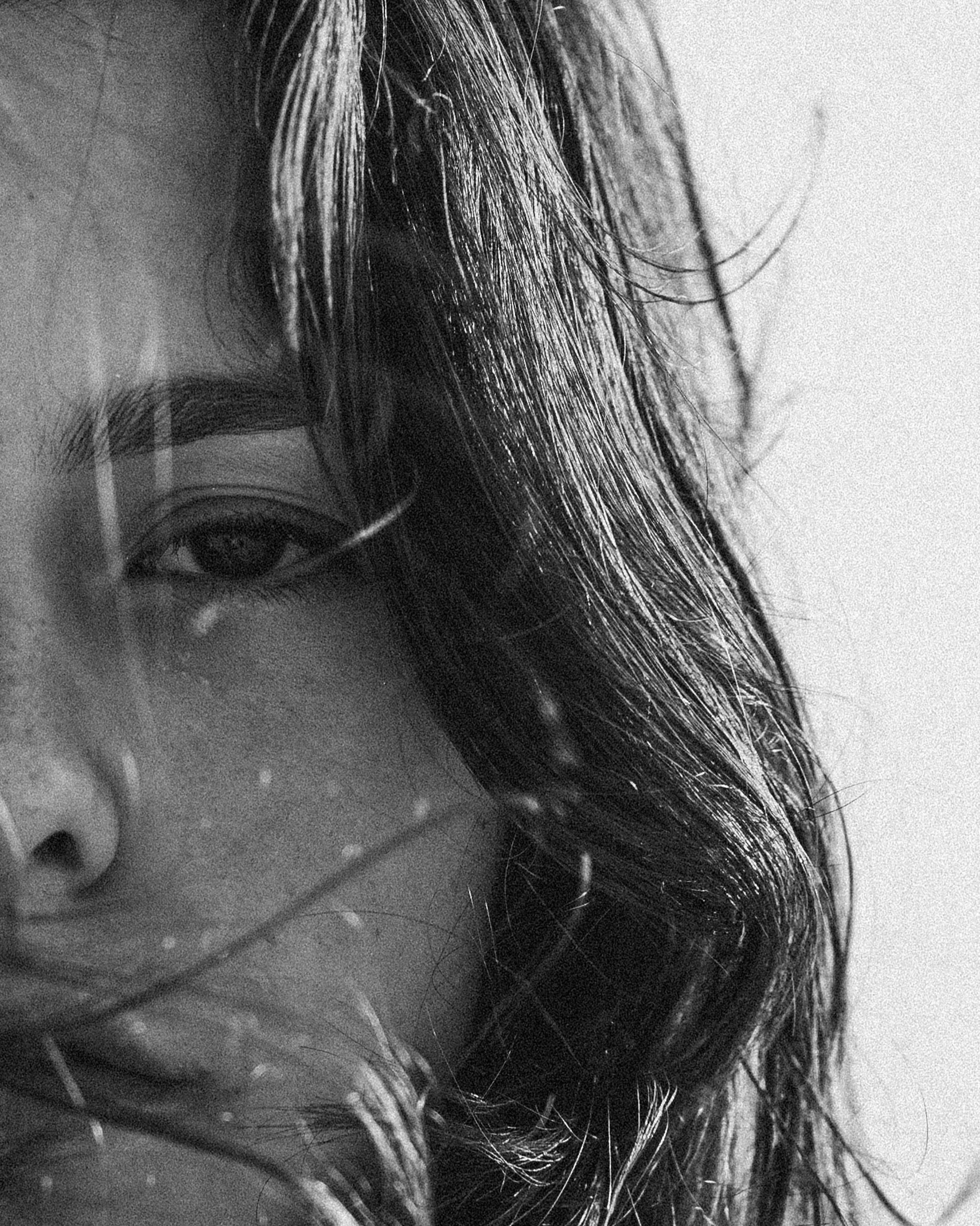 Close-up black and white portrait of a woman's face, showing one eye and part of her nose, with wet curly hair covering part of her face.