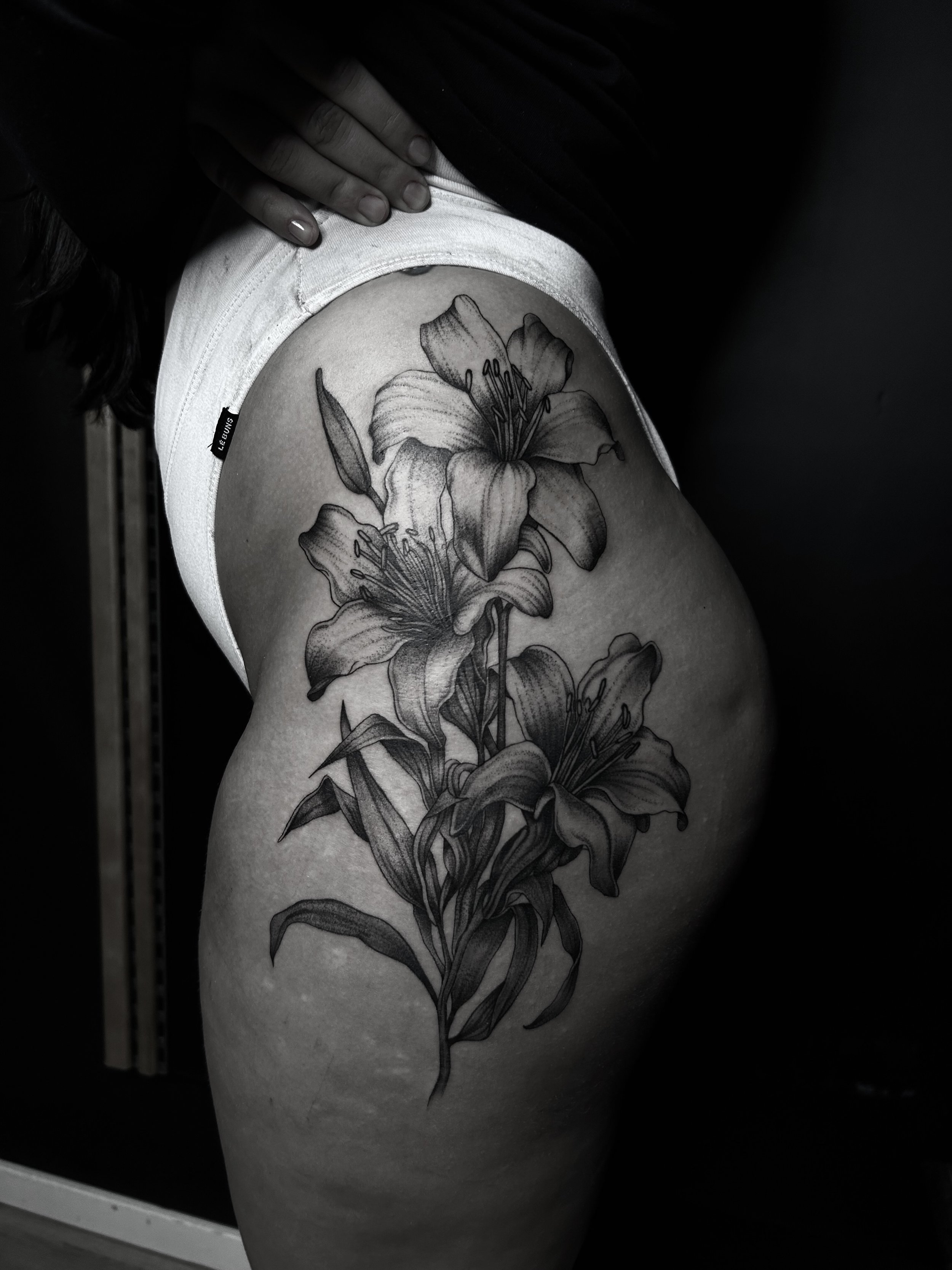 Stor tatuering av blommor på en persons lår, tagen i svartvitt.