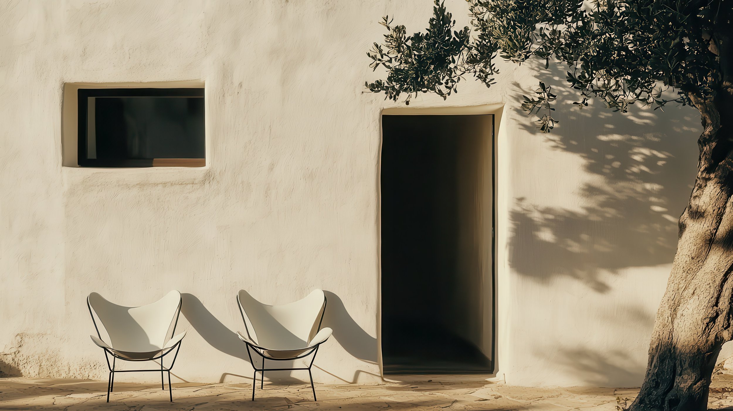 Weiße Wand mit kleiner quadratischer Fensterscheibe, zwei weiße Sessel mit schwarzem Gestell, Schatten eines Baumes auf der Wand und einem offenen schwarzen Türrahmen