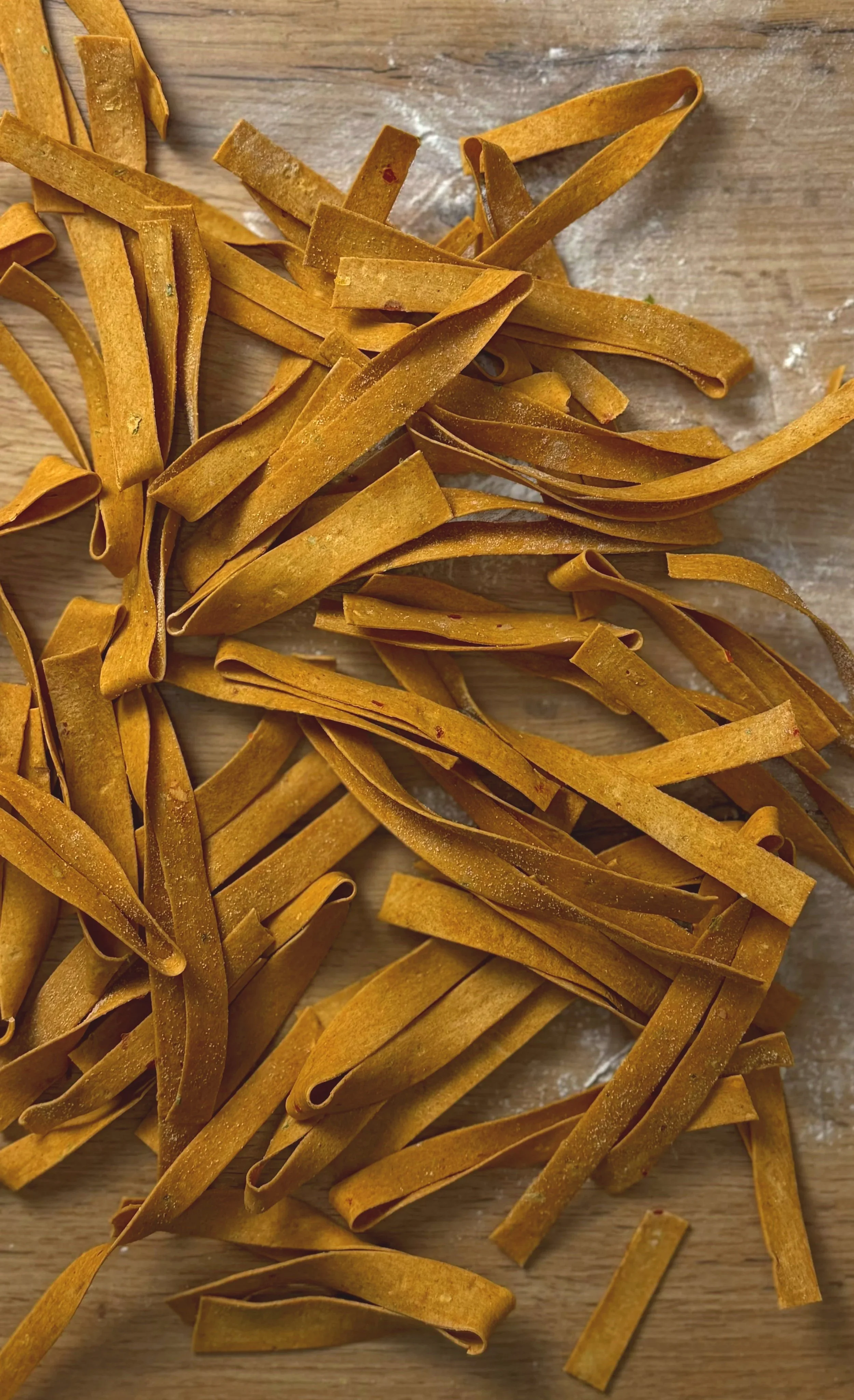 Bunte, flache Nudeln, vermutlich Tagliatelle, auf einem Holzbrett.