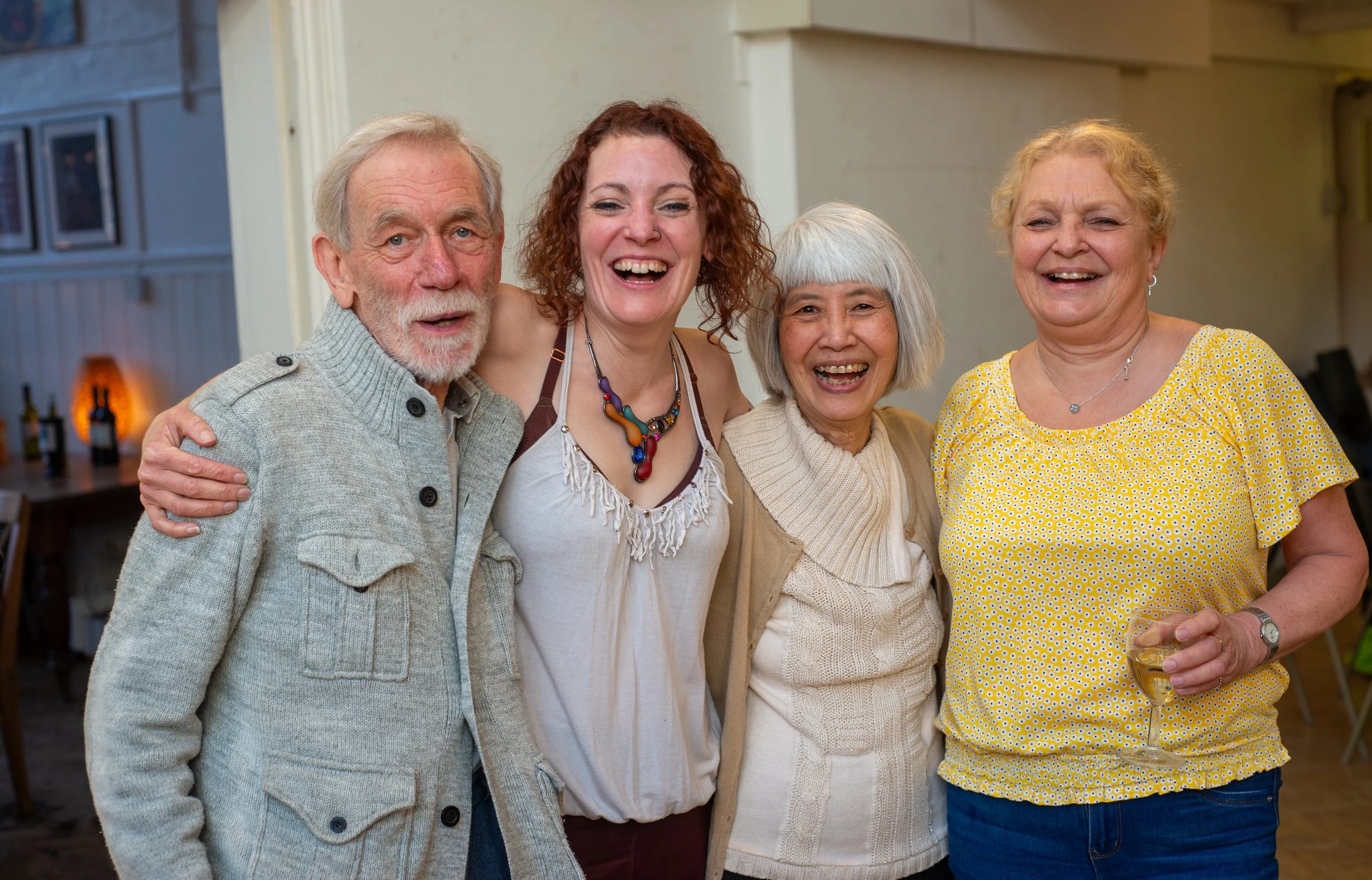 Four people smiling and posing for a photo indoors, one person holding a wine glass.