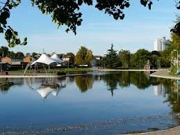 Eastrop Park with a large pond, modern white canopy structure, trees, and high-rise buildings in the background.