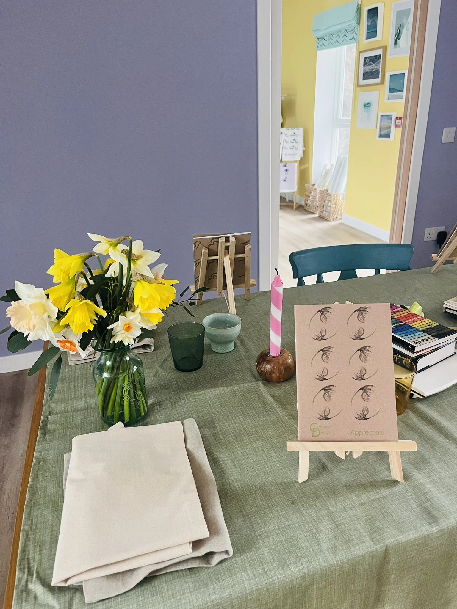 Clement Design print example shown on an easel, on a table with a green table cloth and a vase of daffodils.