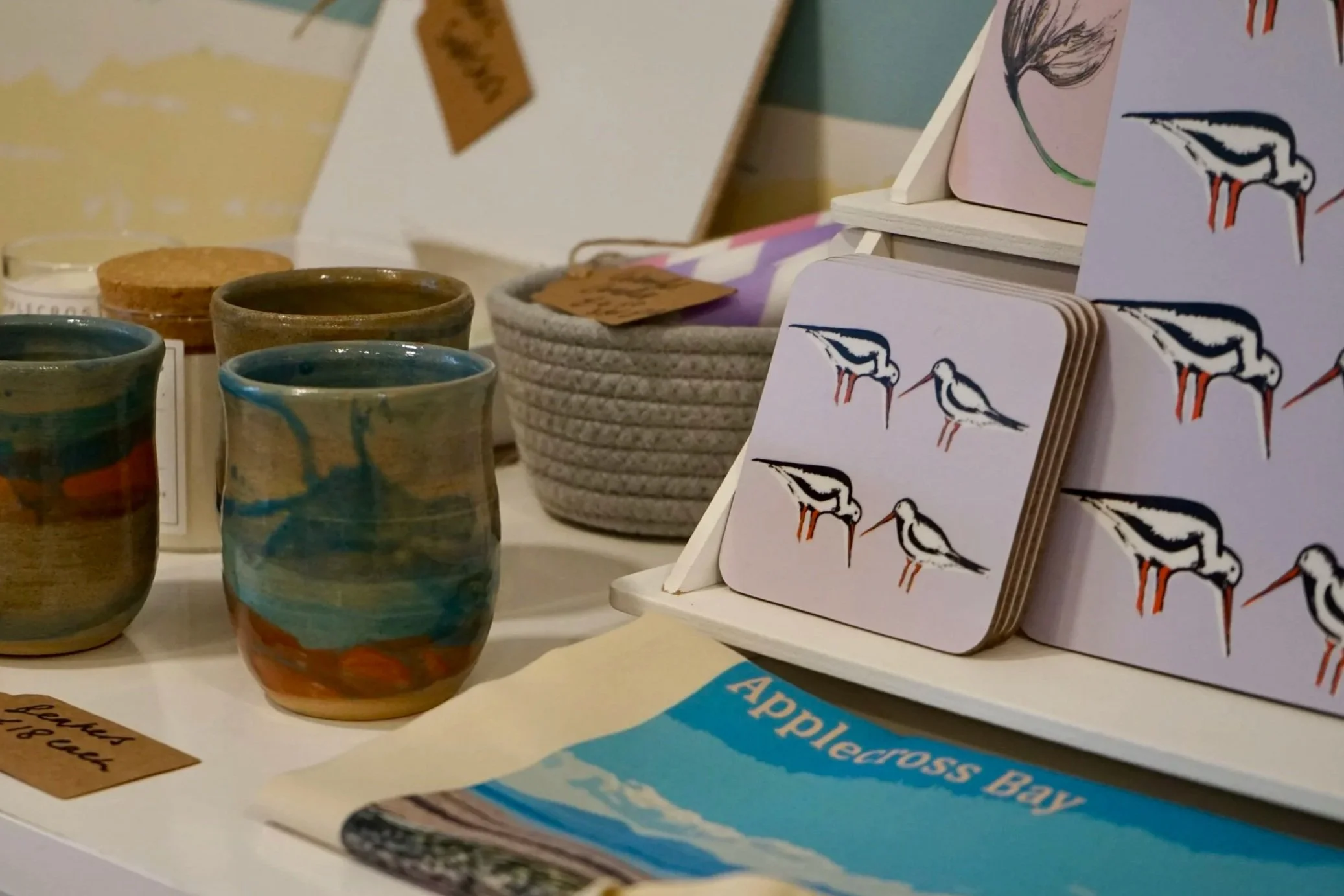 Ceramic mugs with multicolored glaze, small coasters with bird illustrations by Clement Design.