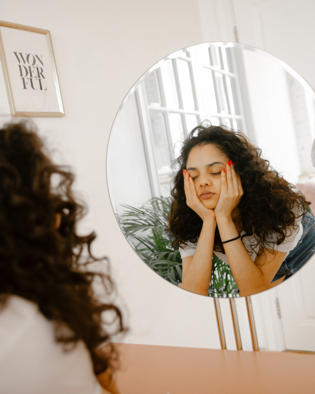 Junge Frau schaut verärgert in den Spiegel, während sie ihre Wangen hält.