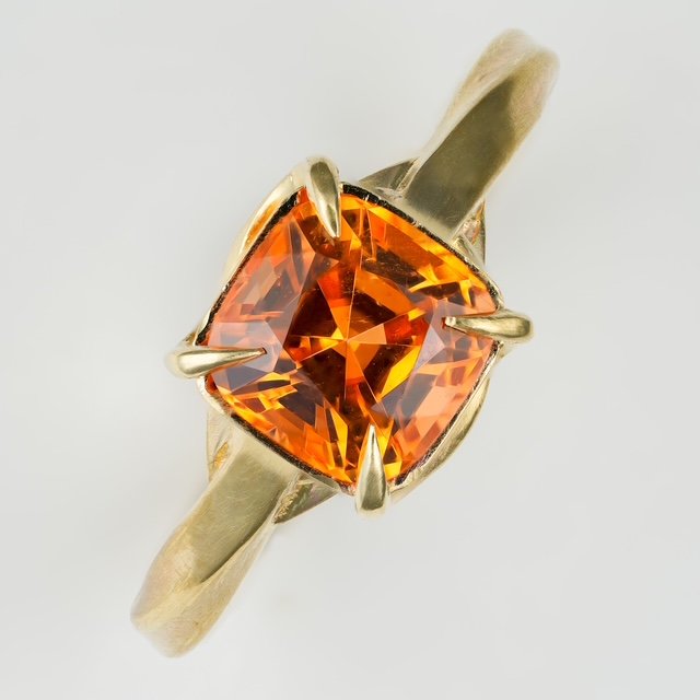 Hand-made 18k fold ring set with a cushion-cut mandarin garnet gemstone, featuring tensioned prongs emerging from the shank