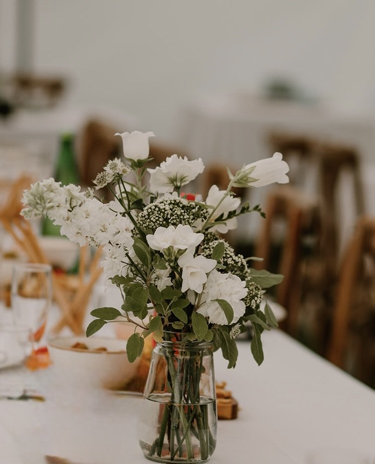 Bouquet of white flowers in a glass jar on a table.