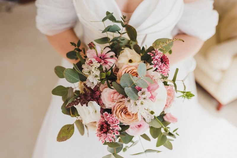 Bride holding a bouquet of pink and white flowers with greenery.