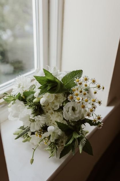 Bouquet of white flowers with green leaves on a windowsill